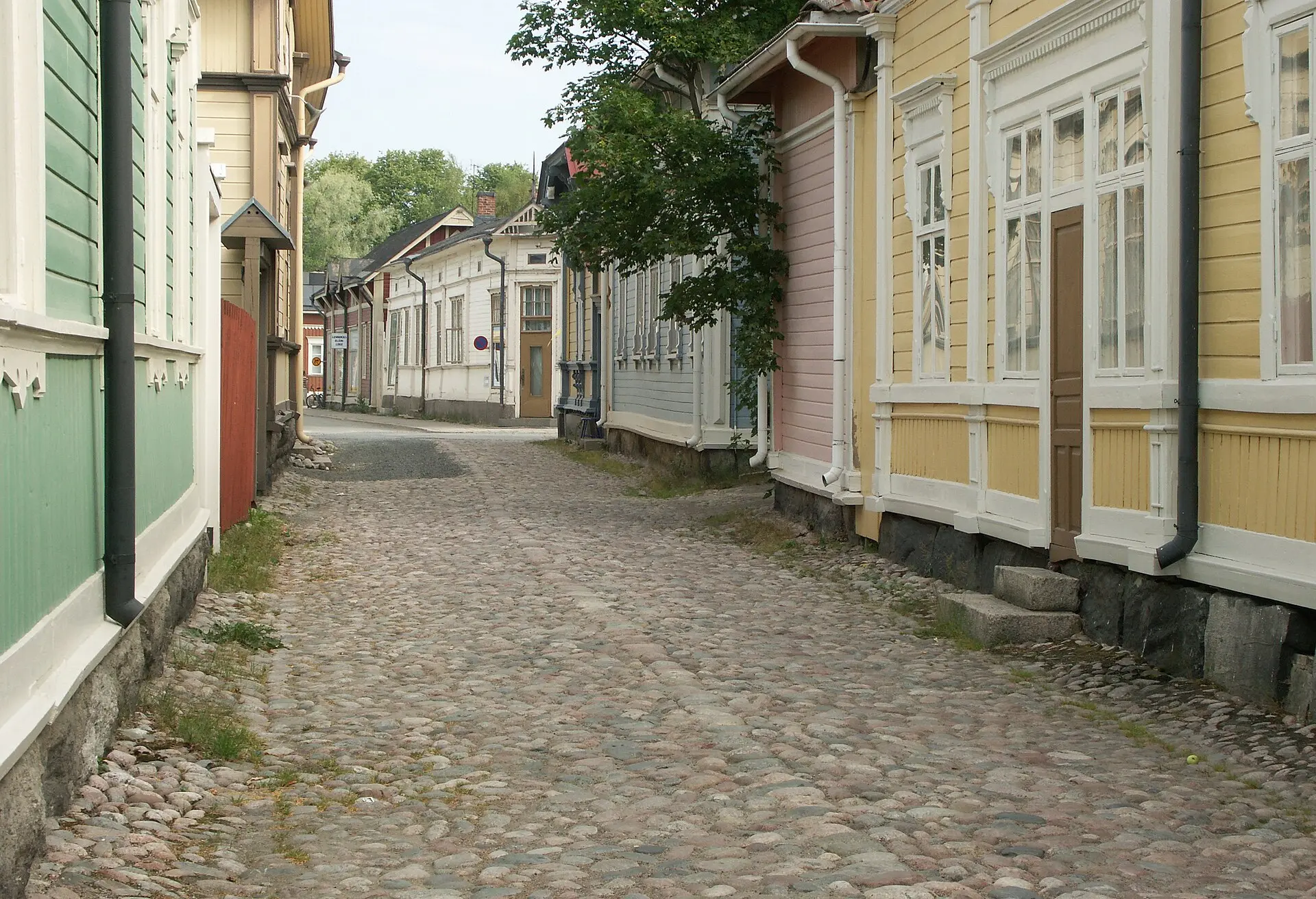 Gasse mit Kopfsteinpflaster in der Altstadt von Rauma zwischen grünen, rosa und gelben Holzhäusern mit weißen Fensterrahmen