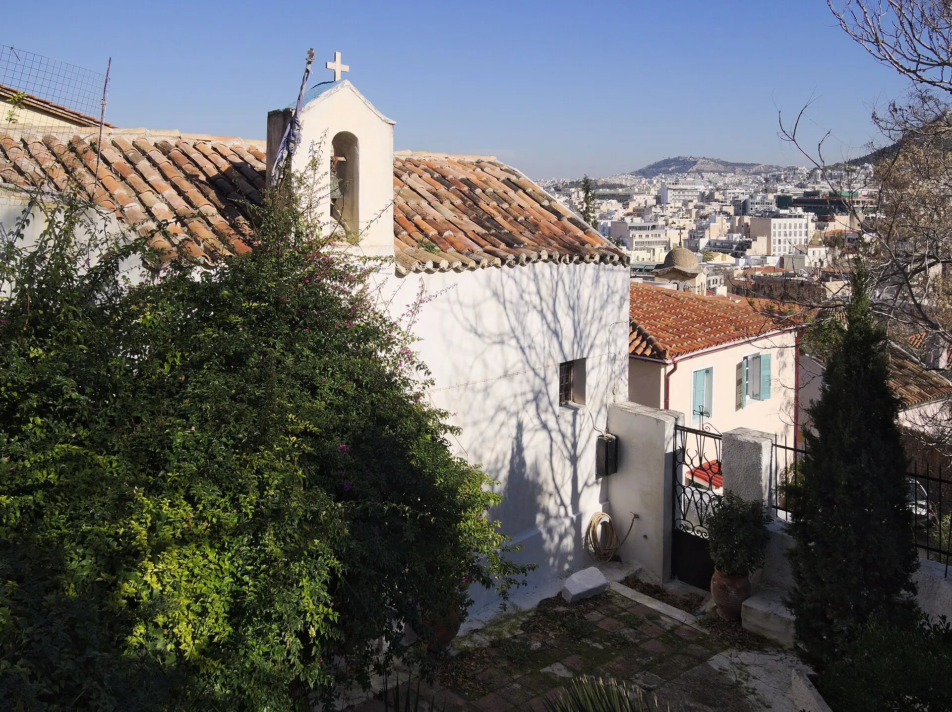 Weiße Kapelle Agios Georgios tou Vrachou in Anafiotika mit Ziegeldach und Glockengiebel, rechts der Blick über die Dächer der Stadt