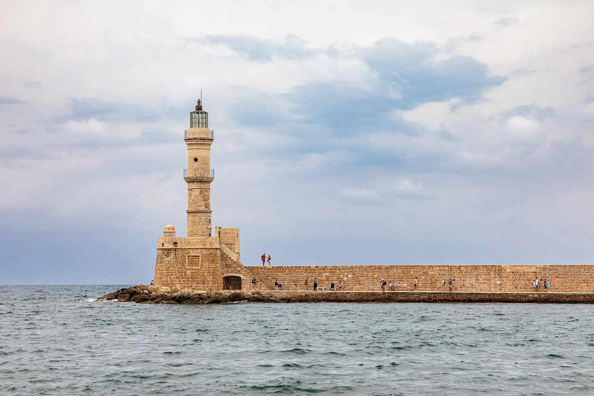 Leuchtturm auf der Hafenmole von Chania auf Kreta, davor offenes Meer, darüber ein bewölkter Himmel
