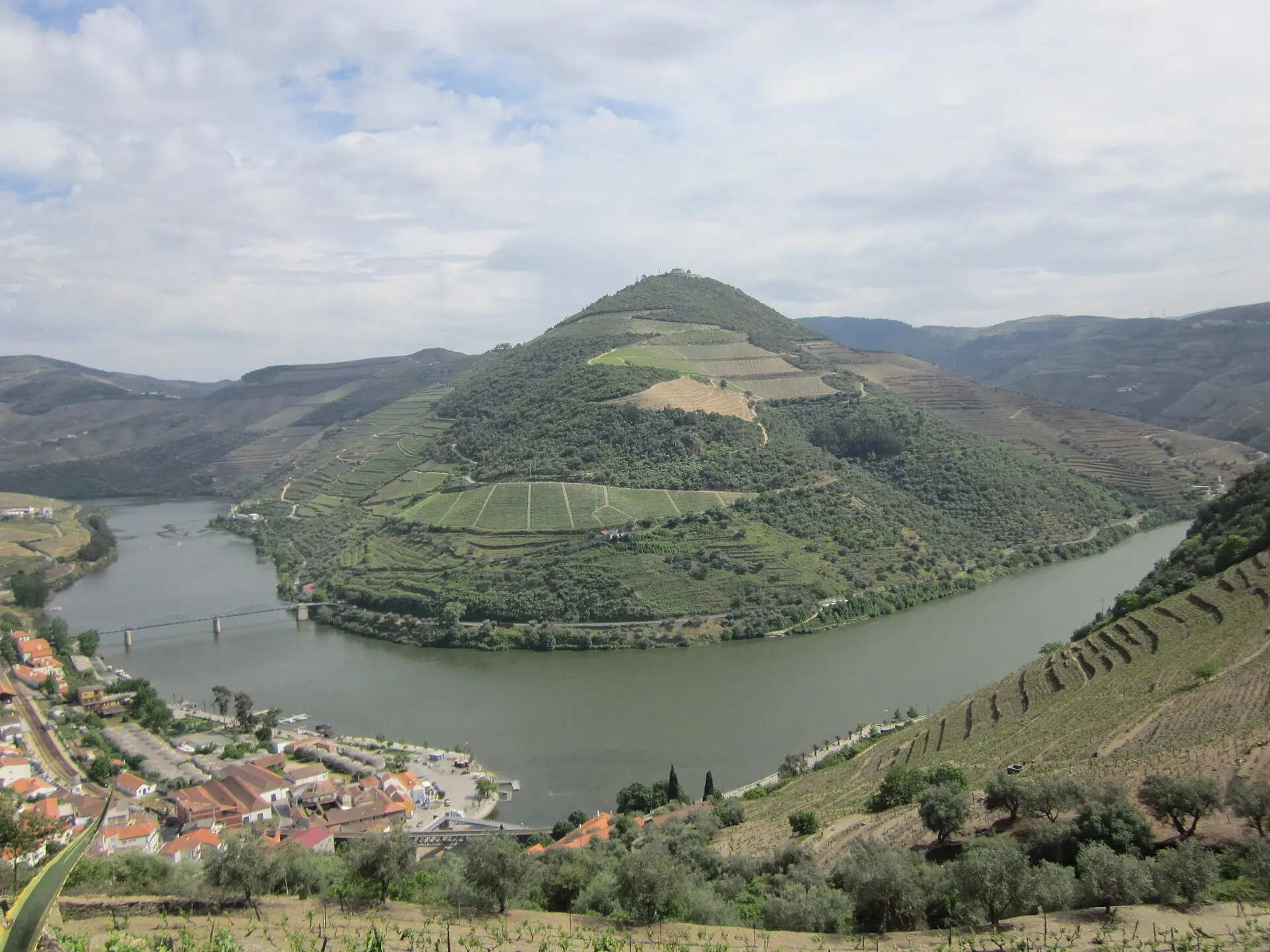 Blick vom Hang auf eine Schleife des Douro bei Pinhão mit Weinterrassen, links unten die Häuser von Pinhão und eine Eisenbrücke