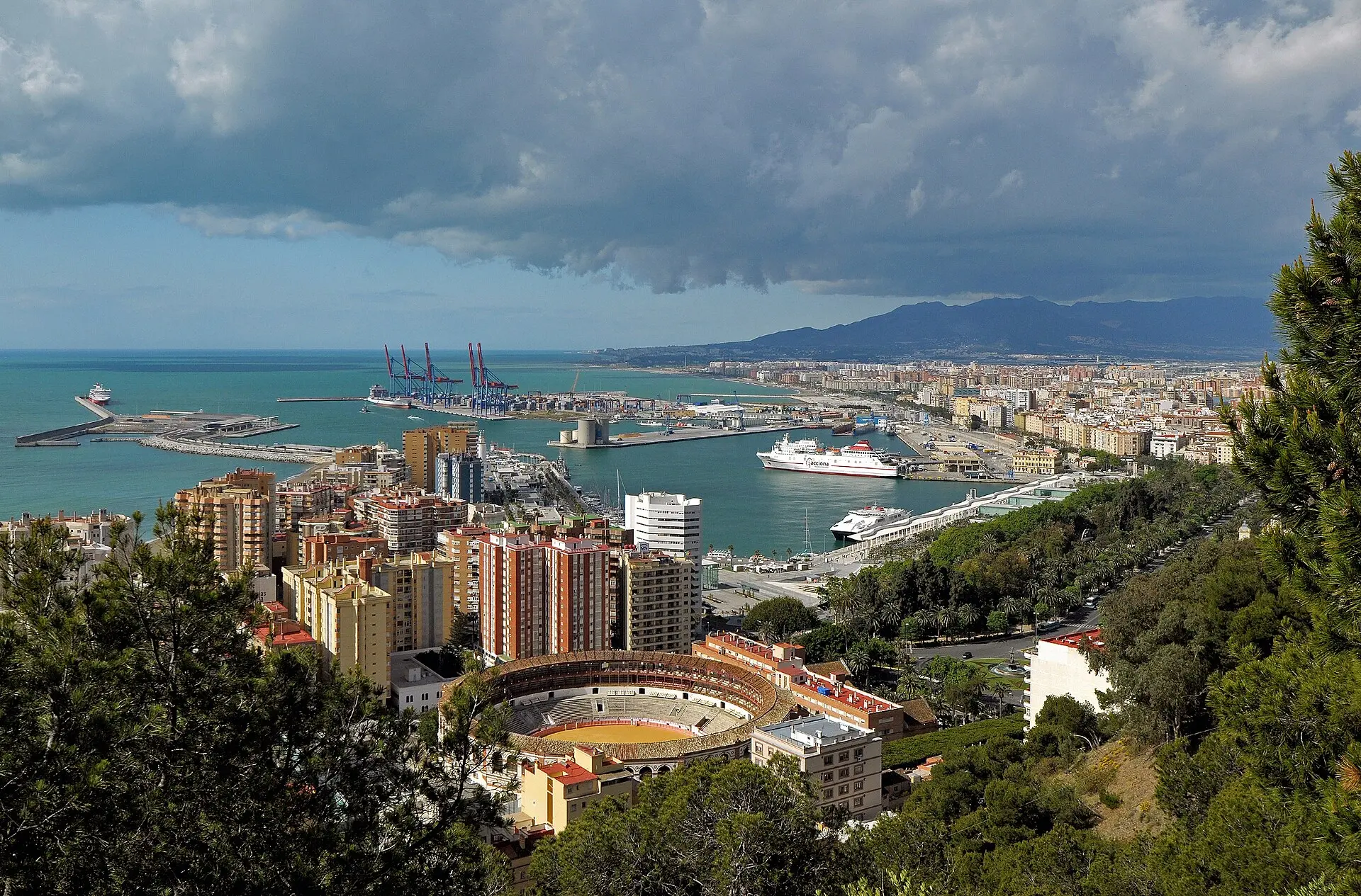 Blick vom Castillo de Gibralfaro auf die Stierkampfarena La Malagueta, Hochhäuser und den Hafen mit Containerkränen und Fähren