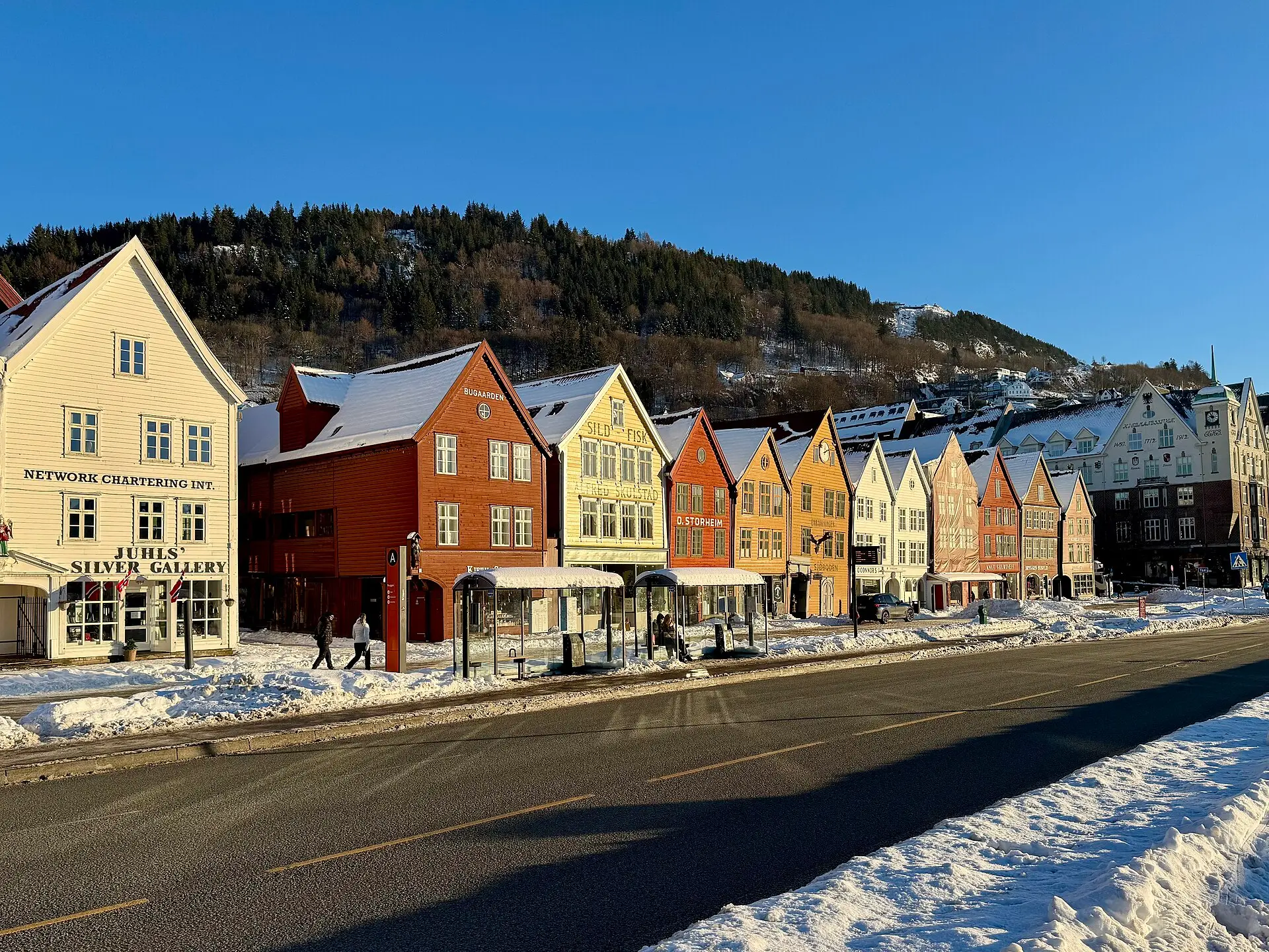 Spitzgieblige Holzhäuser in Rot, Ocker, Gelb und Weiß an der Hafenzeile Bryggen in Bergen, Schnee auf den Dächern