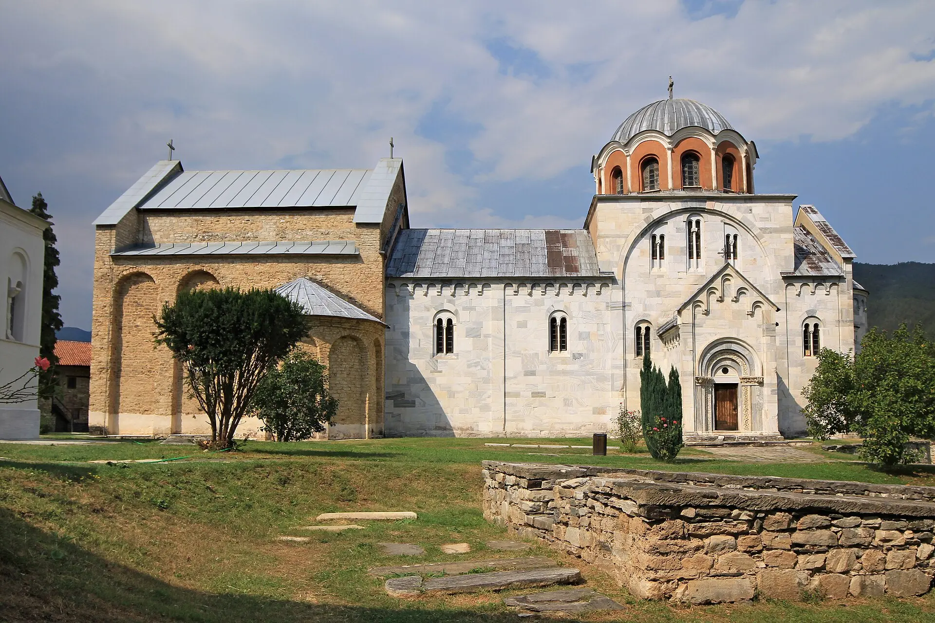 Muttergotteskirche im Kloster Studenica: weiße Marmorfassade, Kuppel auf rot-weißem Tambour, davor Rasen und niedrige Mauerreste