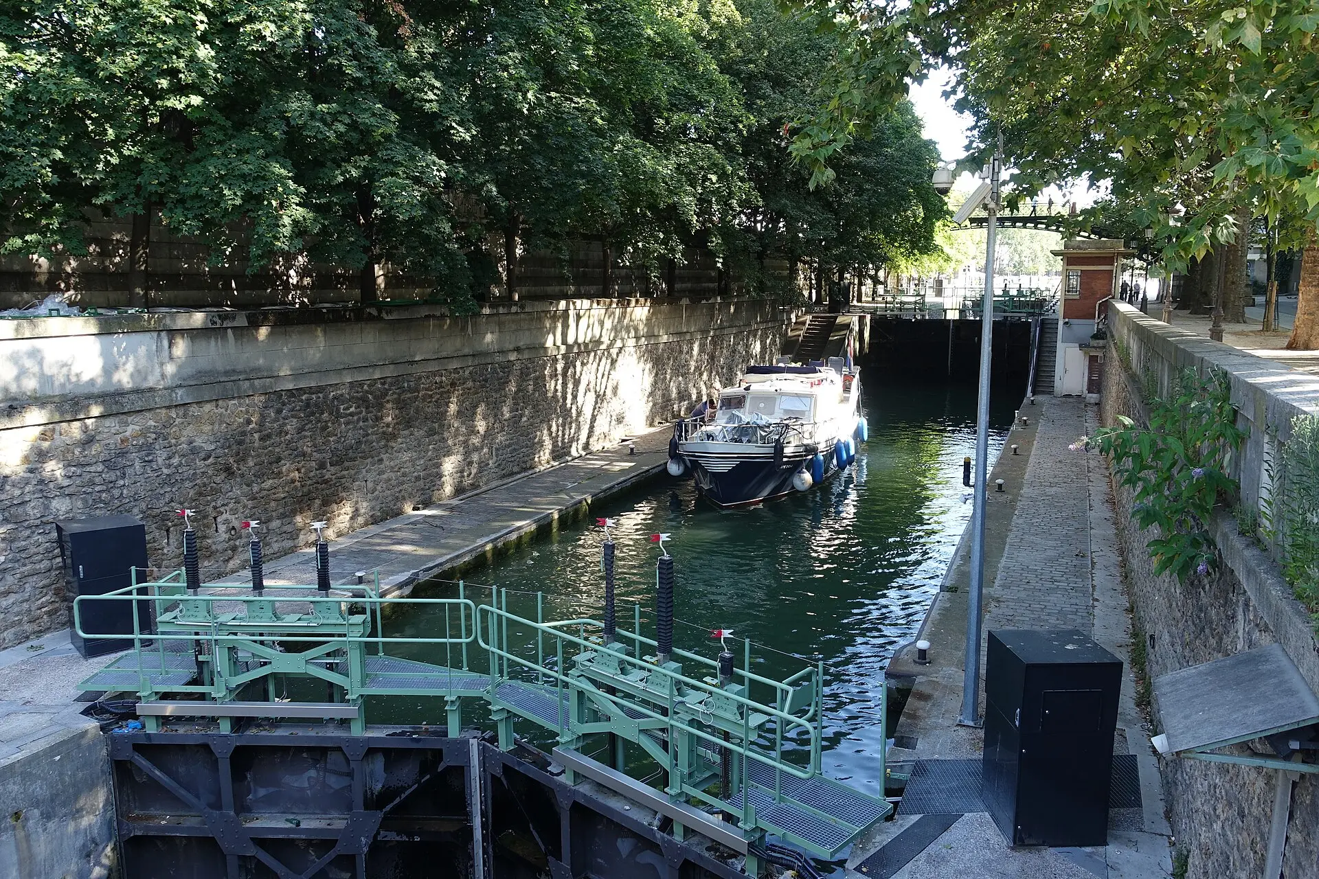 Schleuse am Canal Saint-Martin mit grünen Stegen, einem Boot in der Schleusenkammer und Bäumen am Ufer an einem Sommermorgen