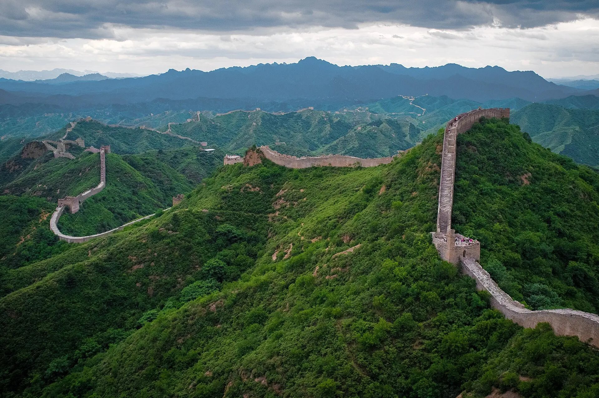 Große Mauer bei Jinshanling: Rechts steigt die Mauer von einem Wachturm steil über einen grünen Bergrücken an, links weitere Abschnitte