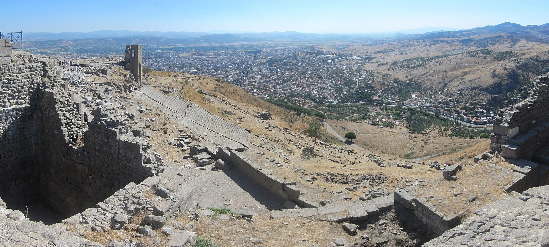 Blick vom Burgberg von Pergamon auf das steile Theater mit Sitzreihen am Hang, dahinter die Stadt Bergama und die Ebene