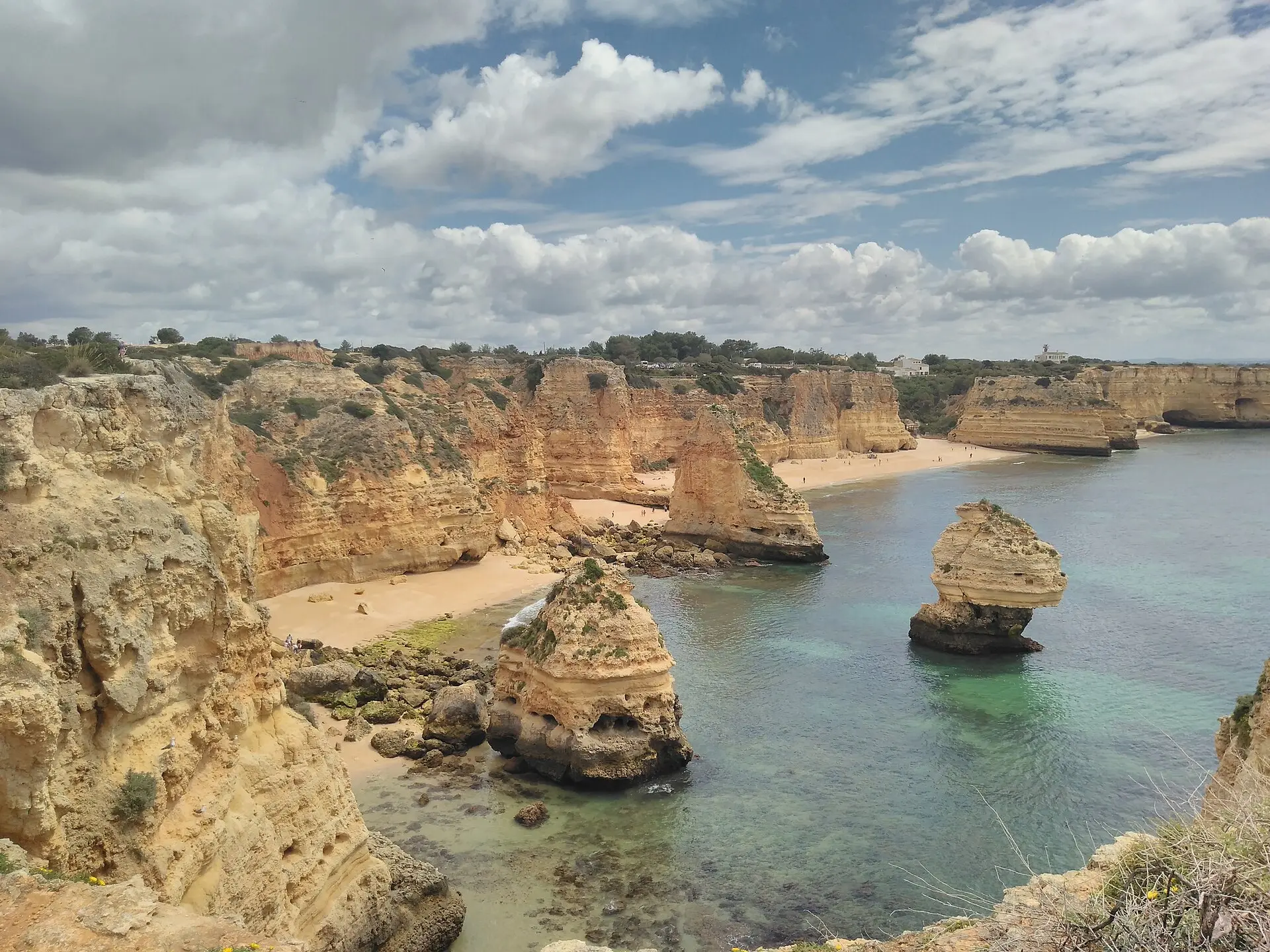 Blick von der Klippe auf die Praia da Marinha mit gelben Kalkfelsen, Sandbuchten und zwei Felsnadeln im türkisfarbenen Wasser