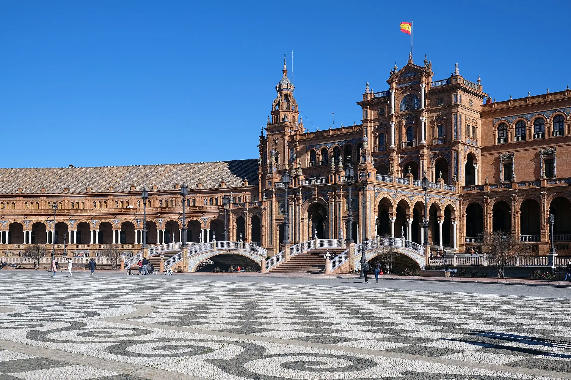 Plaza de España in Sevilla: Backsteinbau mit Arkaden und Turm, Brücken mit weißen Keramikgeländern, davor gewelltes Pflaster