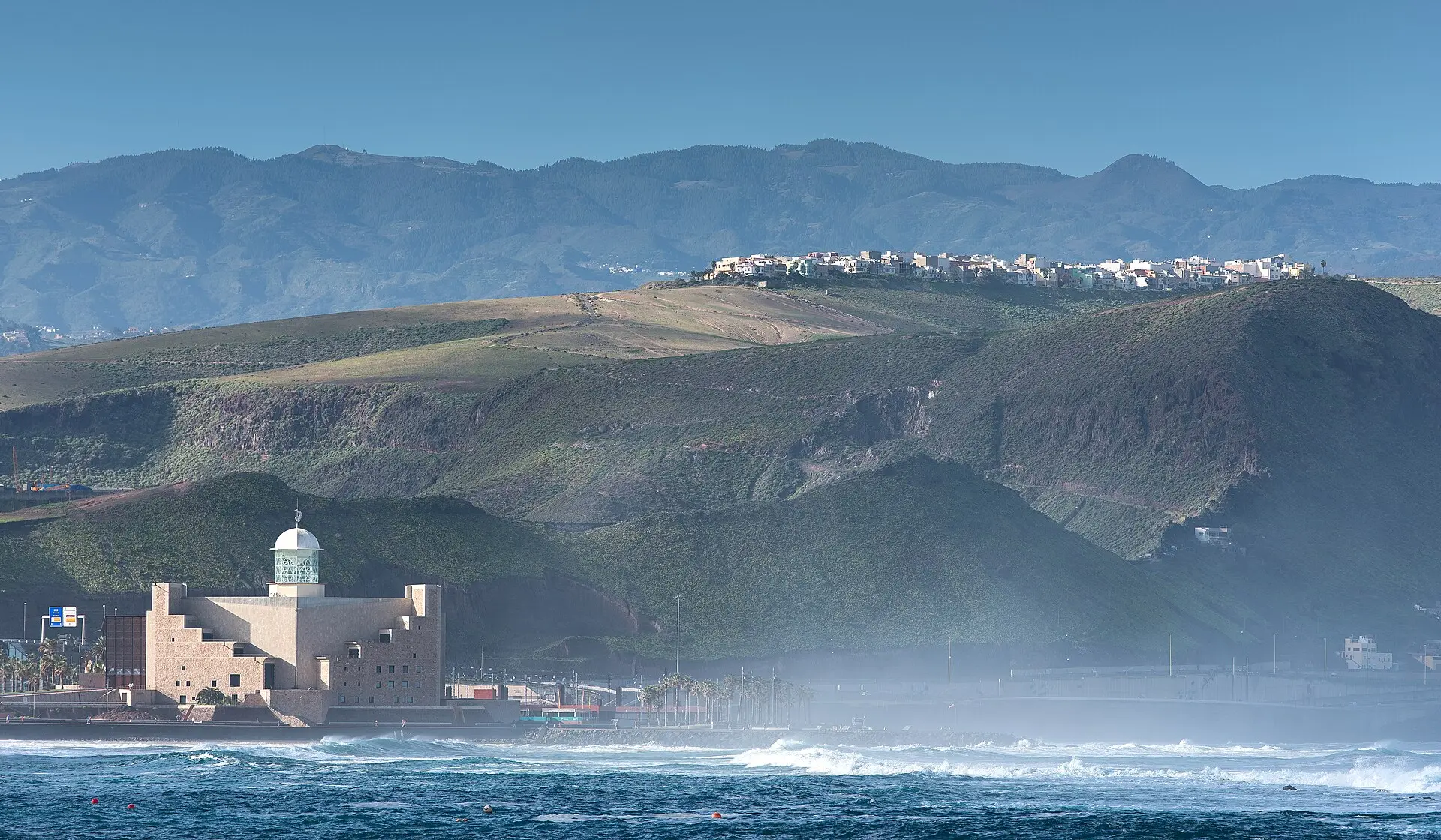 Brandung am Ende der Playa de Las Canteras in Las Palmas mit dem Auditorio Alfredo Kraus, dahinter grüne Hügel