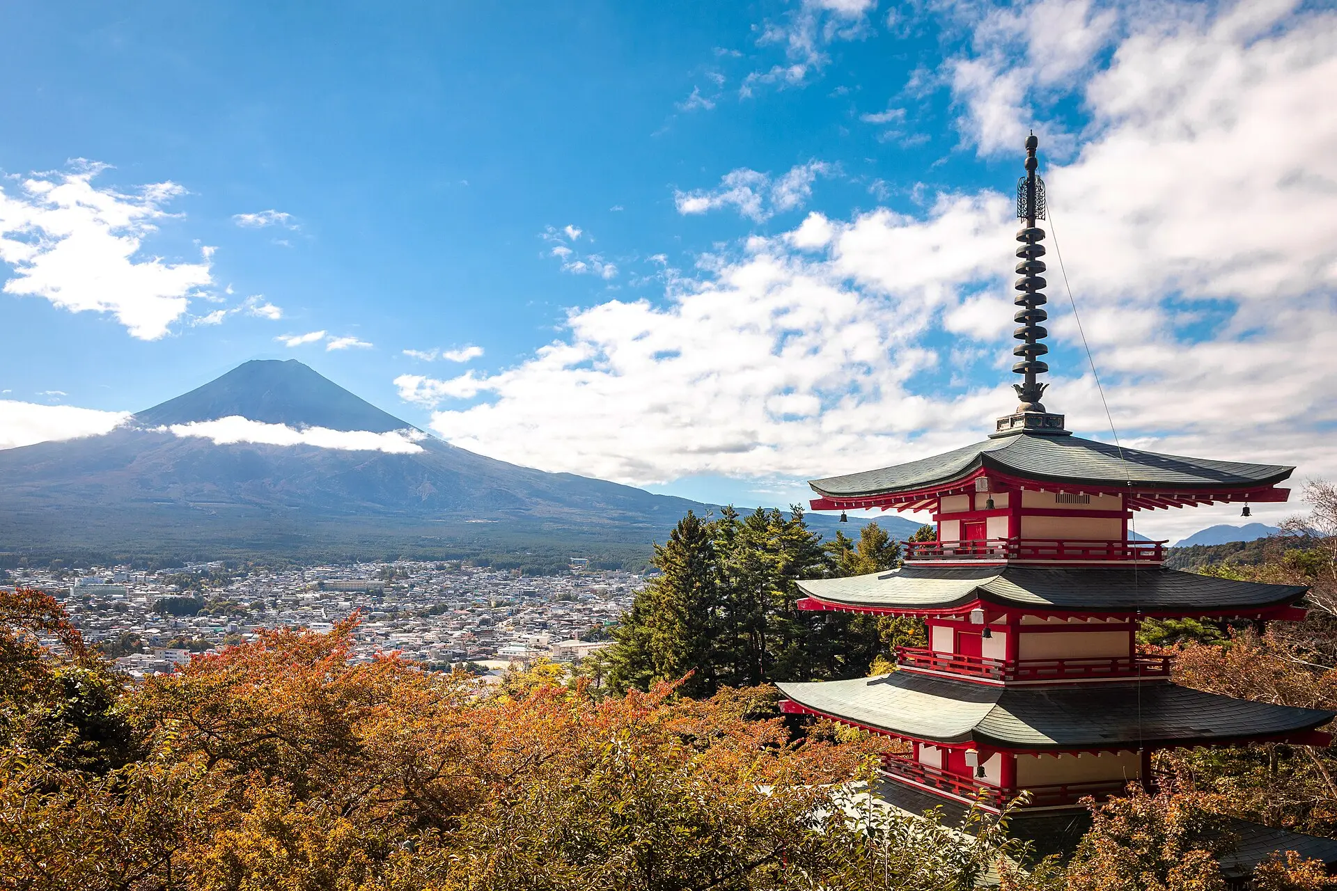 Rote Chureito-Pagode rechts, links dahinter der Fuji mit Wolkenband, unten die Häuser von Fujiyoshida und oranges Herbstlaub