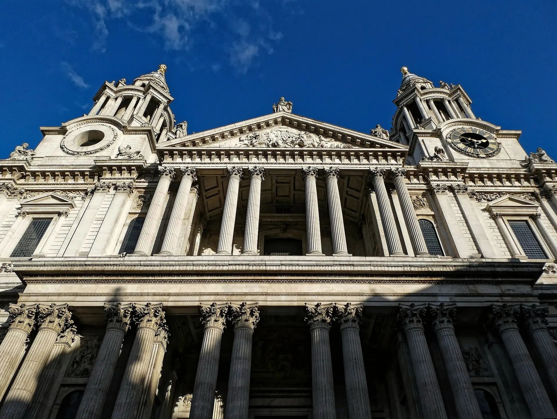 Westfassade der St Paul's Cathedral mit Säulenportikus und zwei Westtürmen, einer davon mit Uhr, vor tiefblauem Himmel