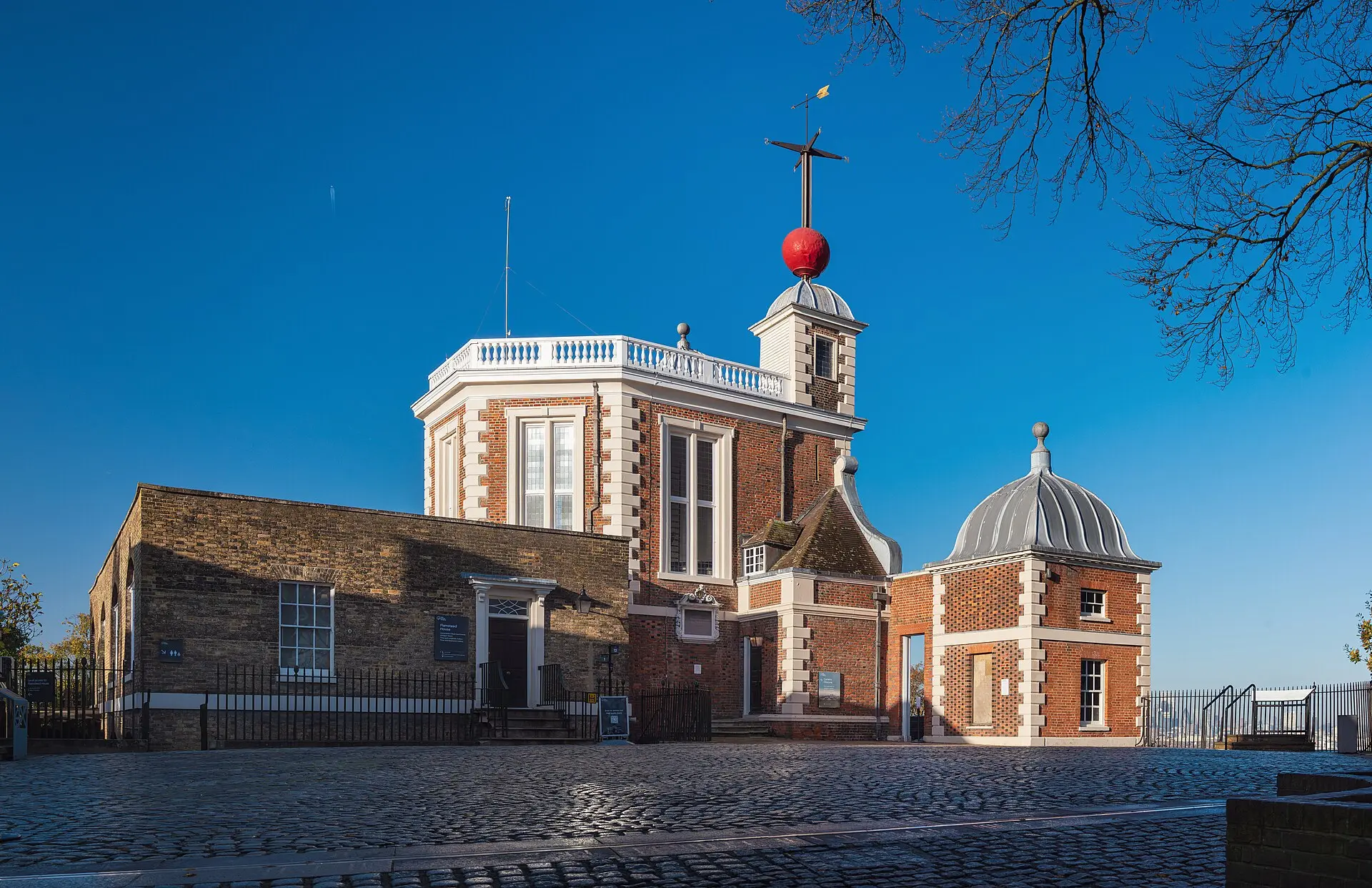 Flamsteed House des Royal Observatory Greenwich aus rotem Backstein mit roter Zeitkugel auf dem Dach, davor Kopfsteinpflaster