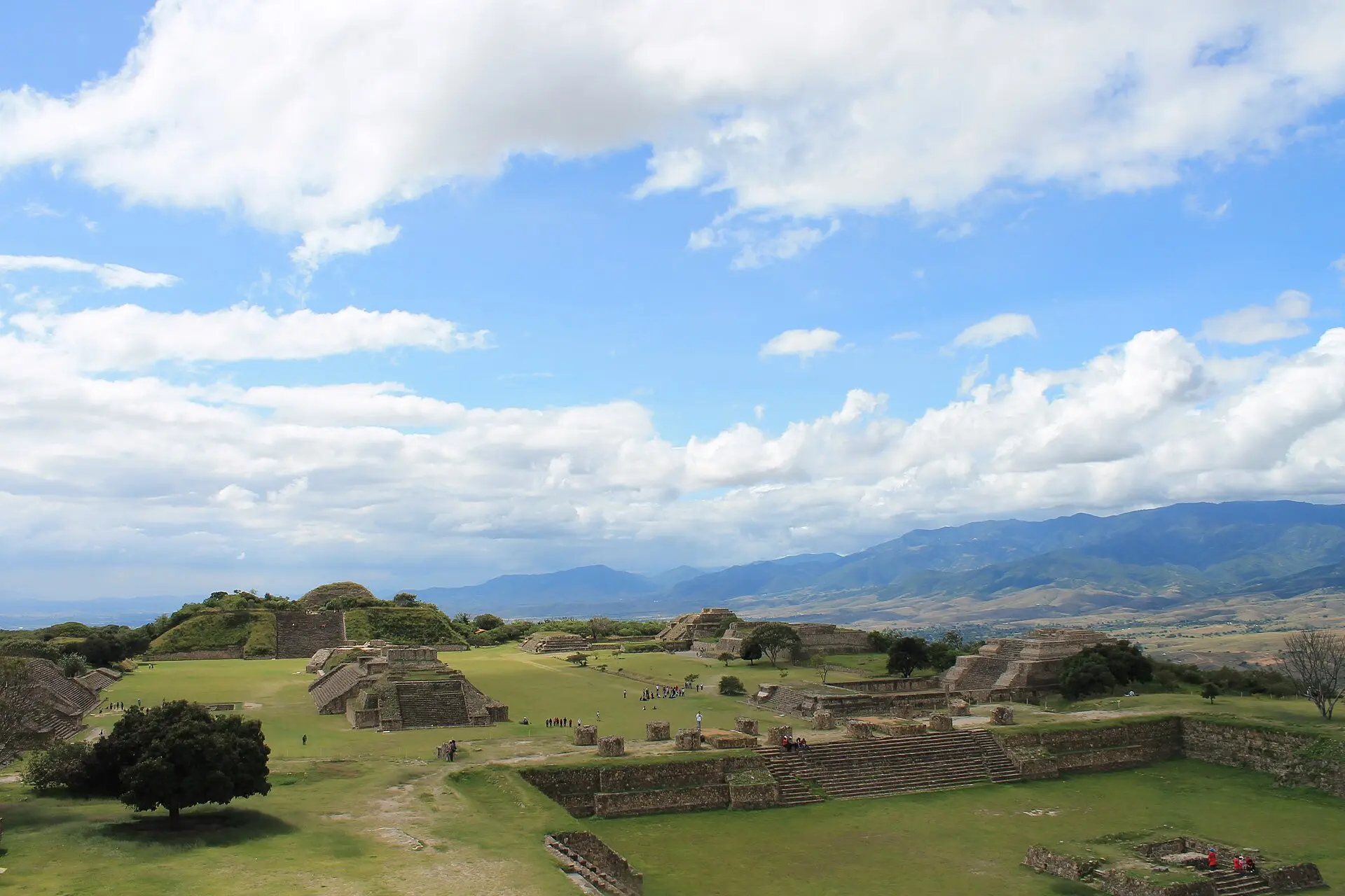 Blick von der Nordplattform über die große Plaza von Monte Albán mit Tempelbauten, dahinter Bergketten unter Wolken