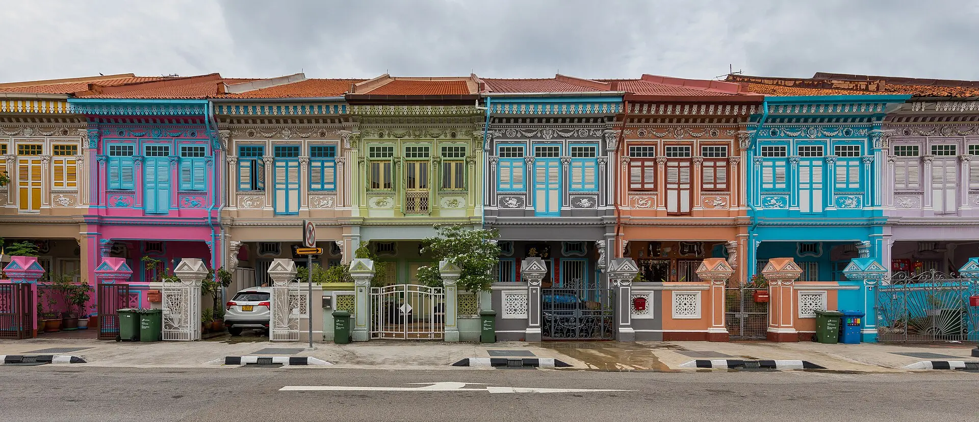 Reihe zweistöckiger Shophouses mit Stuck und Fensterläden, die Fassaden in Pink, Hellgrün, Grau, Orange und Türkis, bedeckter Himmel