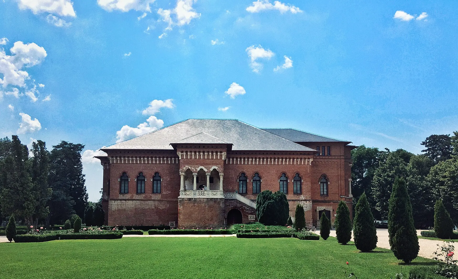 Backsteinpalast Mogoșoaia von vorn mit Loggia und Außentreppe, davor Rasen, Buchsbaumbeete und kegelförmige Nadelbäume