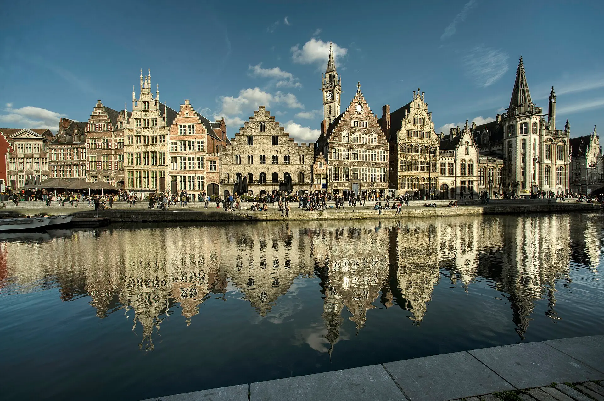 Historische Giebelhäuser an der Graslei in Gent im Abendlicht, gespiegelt im Wasser der Leie, dahinter ein Uhrturm