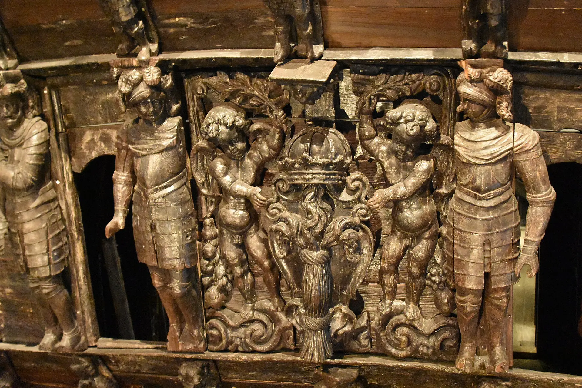 Geschnitzte Holzfiguren am Kriegsschiff Vasa: zwei Krieger in Rüstung und zwei Putten, die ein Wappen mit Krone halten