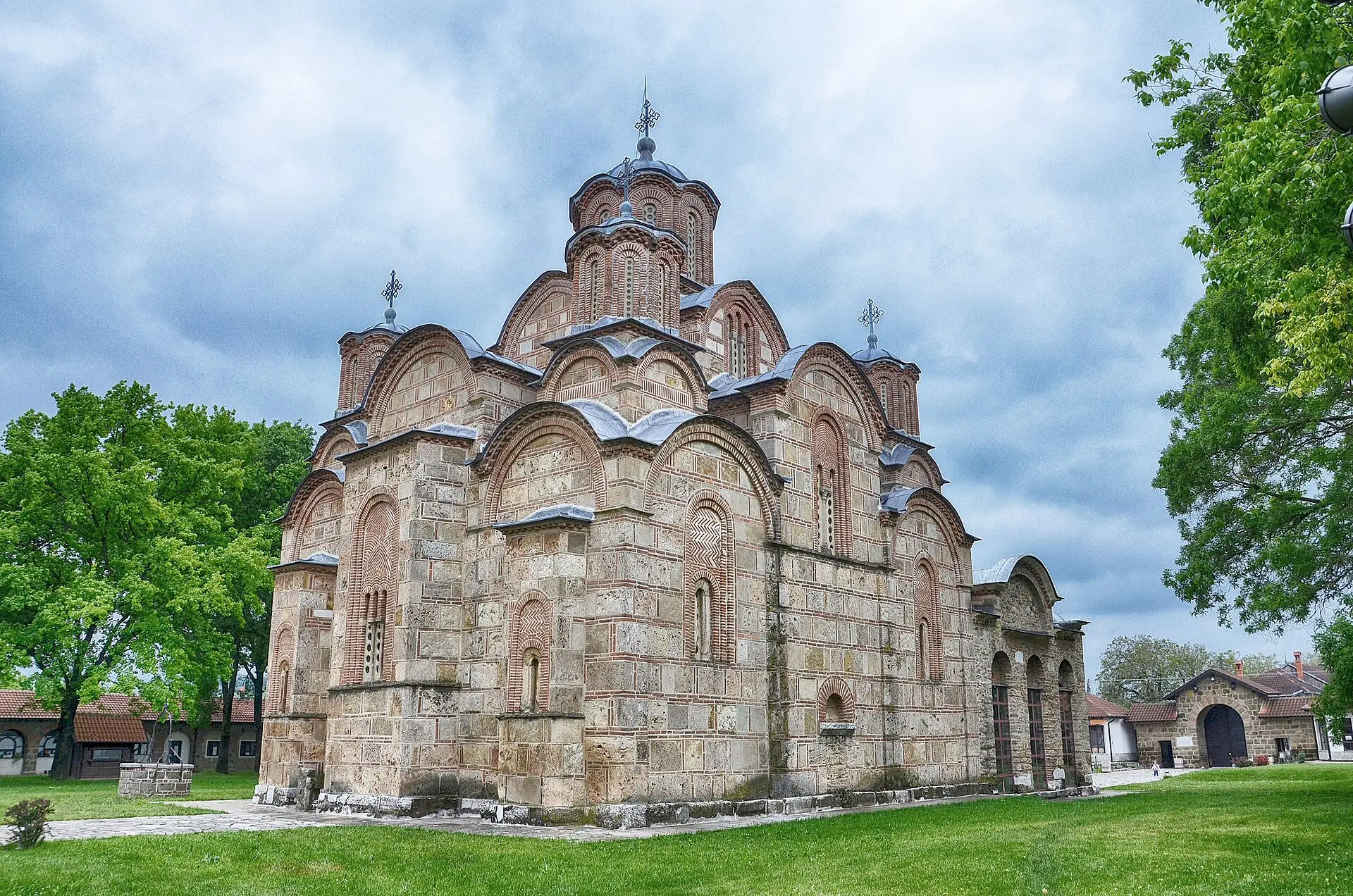 Klosterkirche Gračanica aus hellem Stein mit roten Ziegelbändern, gestaffelten Bögen und fünf Kuppeltürmen, vorn Rasen