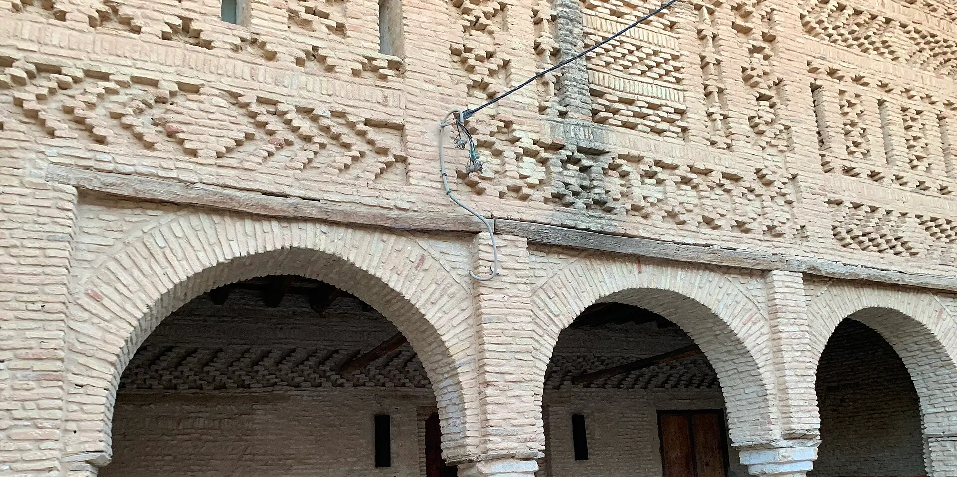 Hauswand in der Altstadt von Tozeur aus hellen Ziegeln mit Rauten- und Zickzackmustern über drei Rundbögen und einem Laubengang
