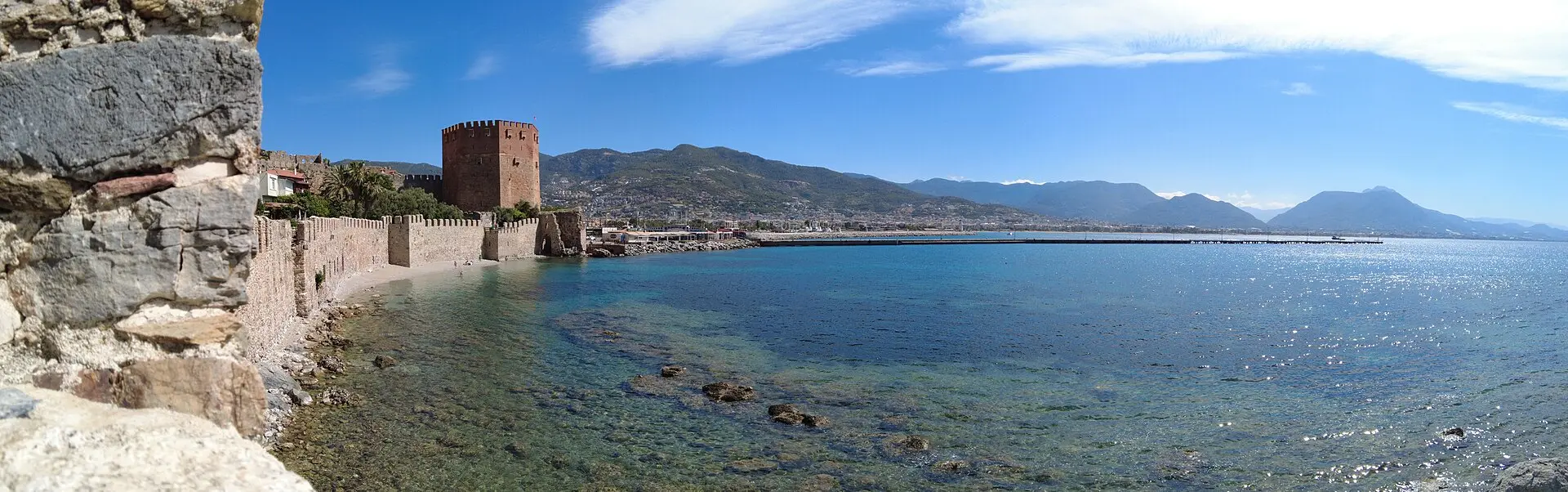 Panorama von Alanya mit dem achteckigen Roten Turm an der Stadtmauer, dem Hafenbecken und Bergen im Hintergrund