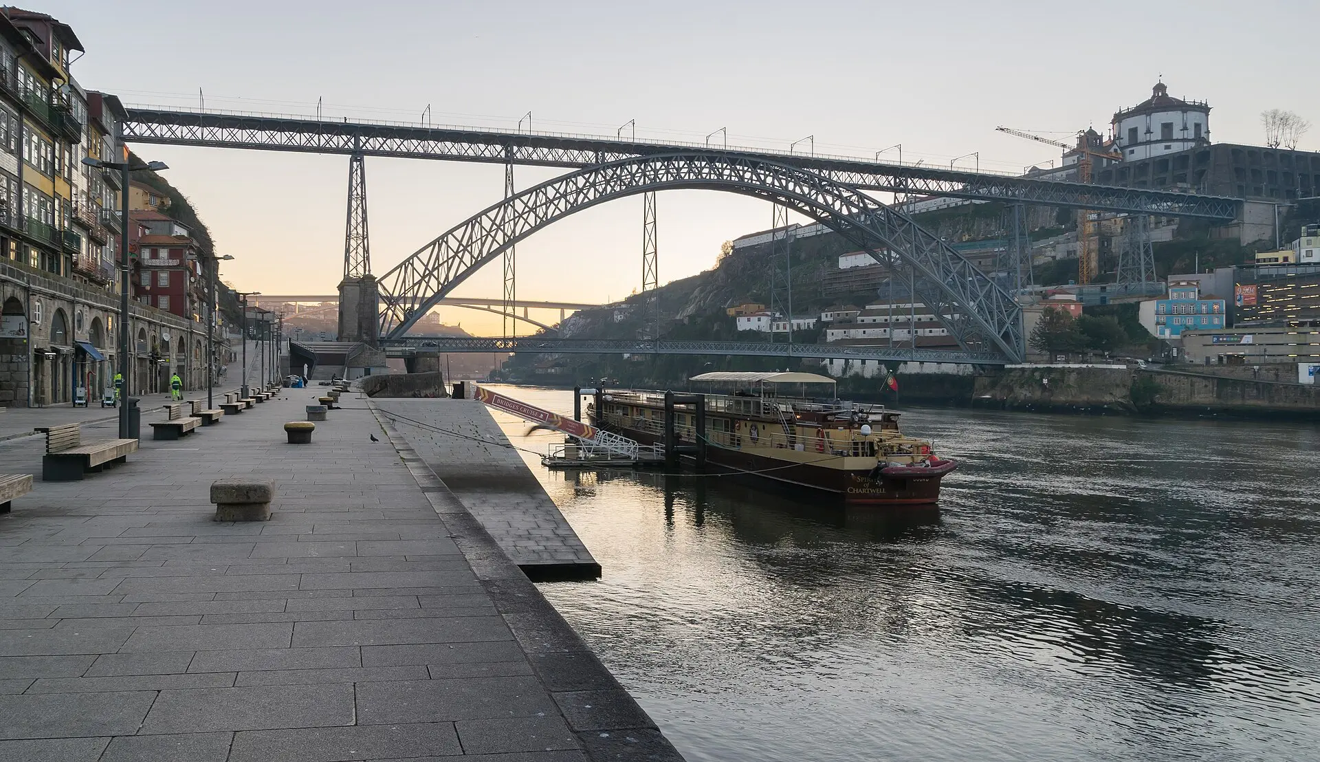 Die Brücke Luís I mit zwei eisernen Fahrbahnen im Morgenlicht, gesehen vom Kai der Ribeira; rechts oben das Kloster Serra do Pilar