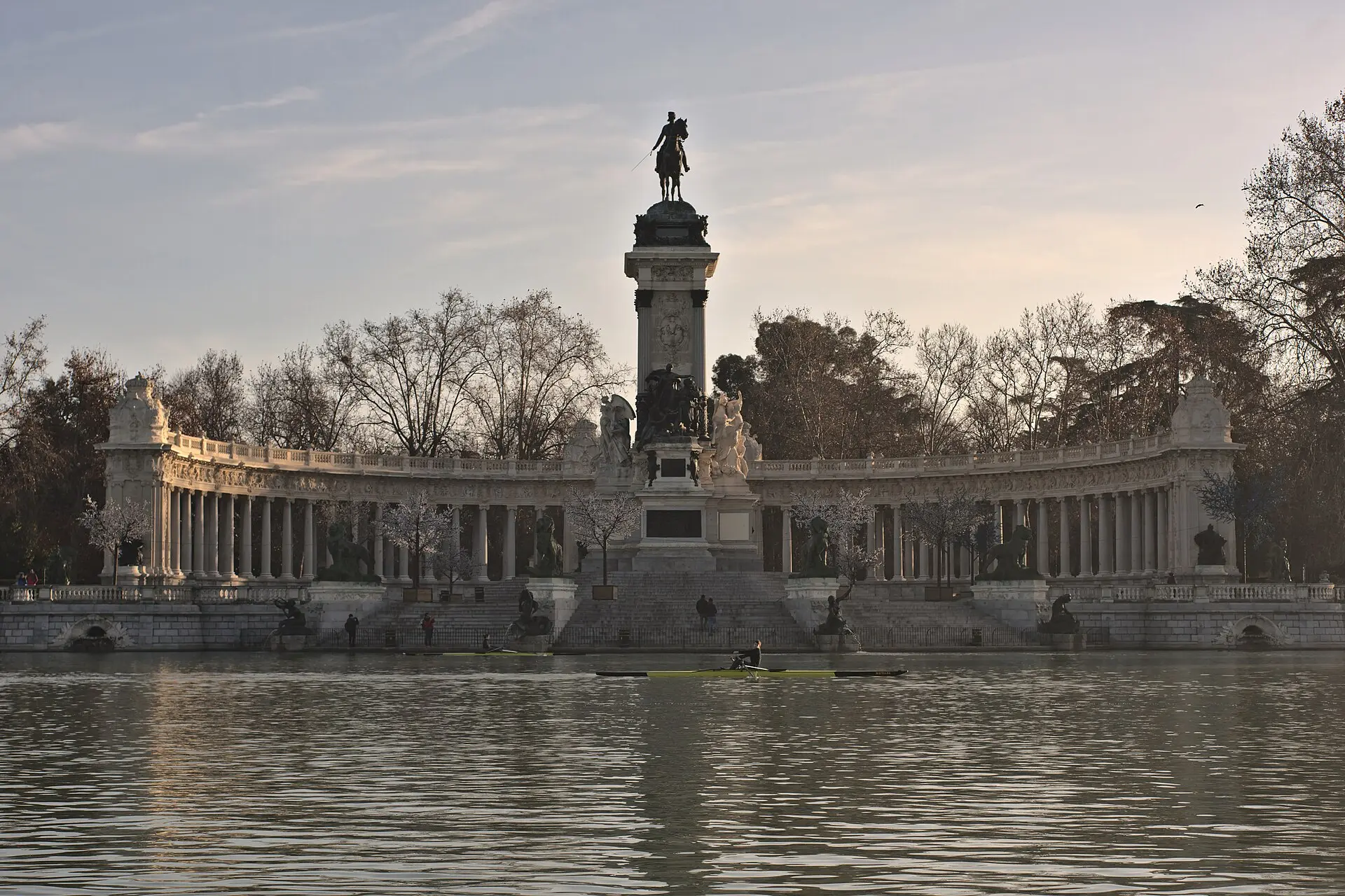 See im Retiro-Park mit dem Denkmal für Alfons XII.: Reiterstatue auf einer Säule vor halbrunder Kolonnade, kahle Bäume, ein Ruderboot