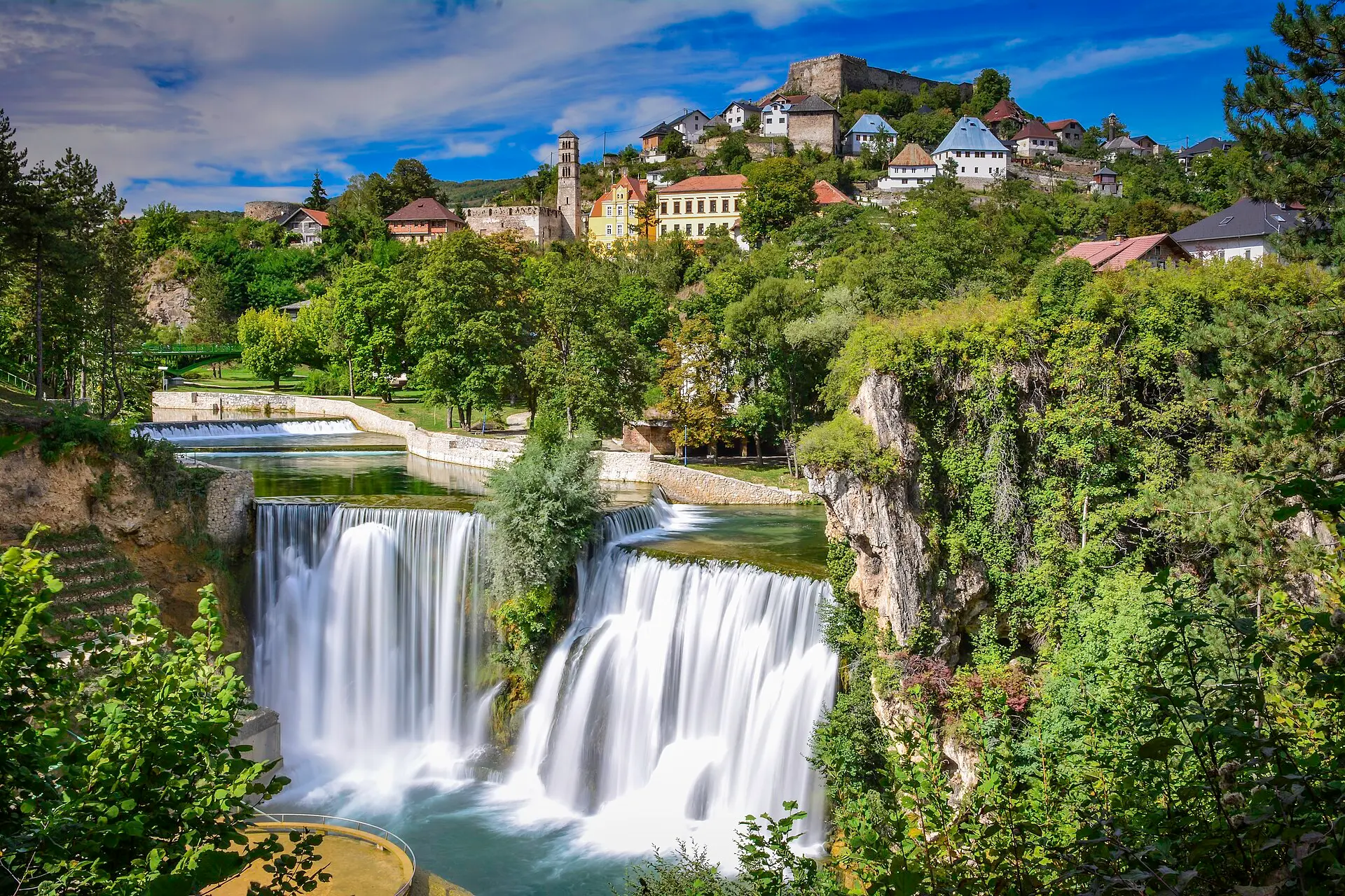 Pliva-Wasserfall in Jajce in zwei Strömen, darüber die Altstadt am Hang mit Glockenturm und Festungsmauern auf dem Hügel