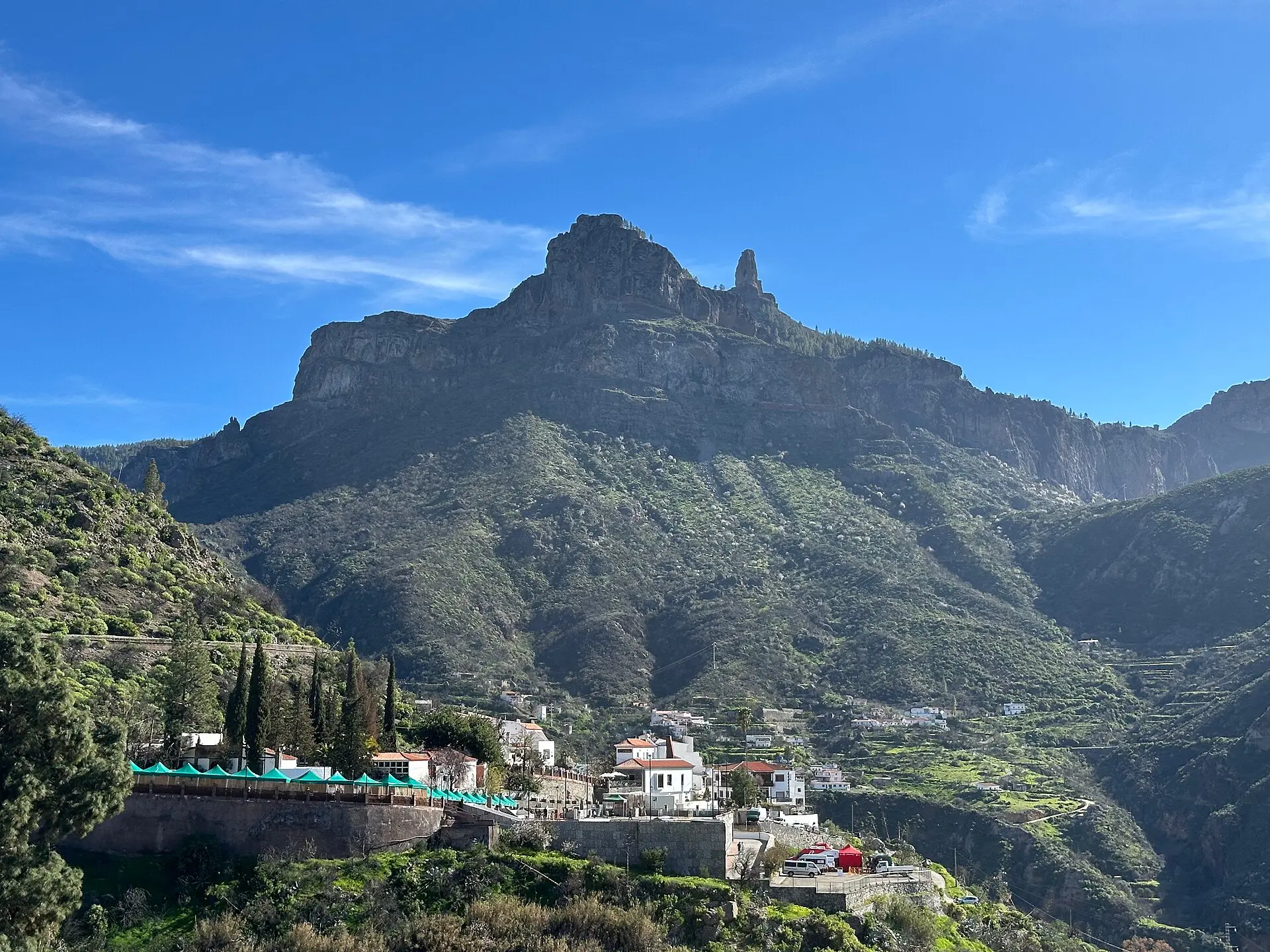 Blick von Tejeda auf den Bergrücken mit dem Felsfinger Roque Nublo, darunter grüne Hänge und weiße Häuser