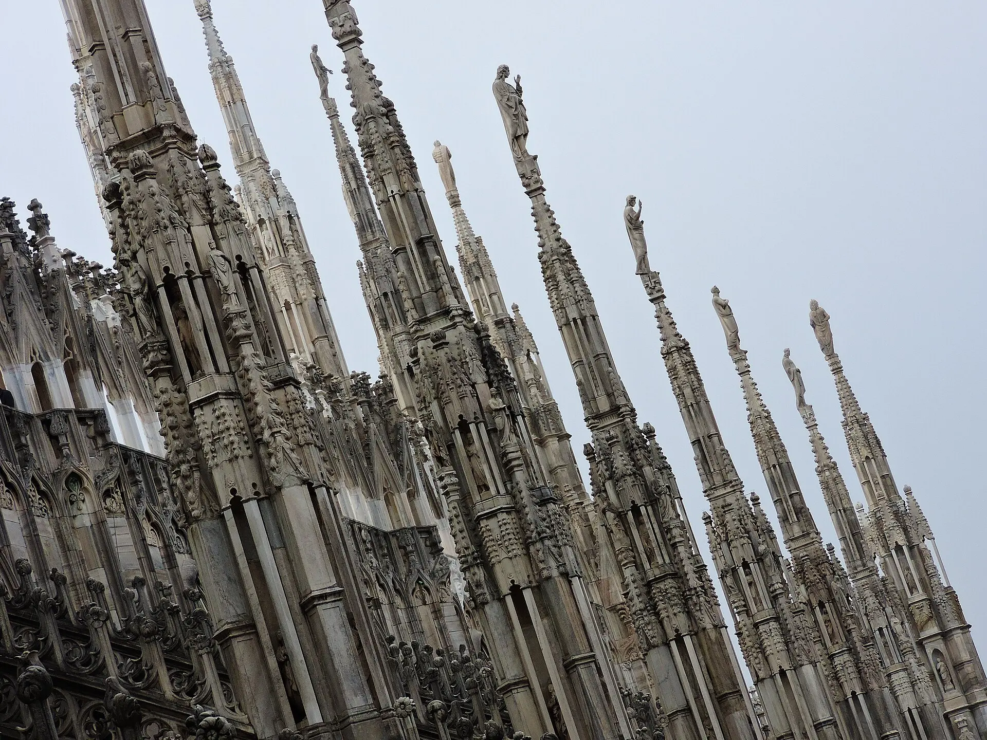 Verzierte Marmorfialen mit Heiligenstatuen auf den Terrassen des Mailänder Doms unter grauem, bedecktem Himmel
