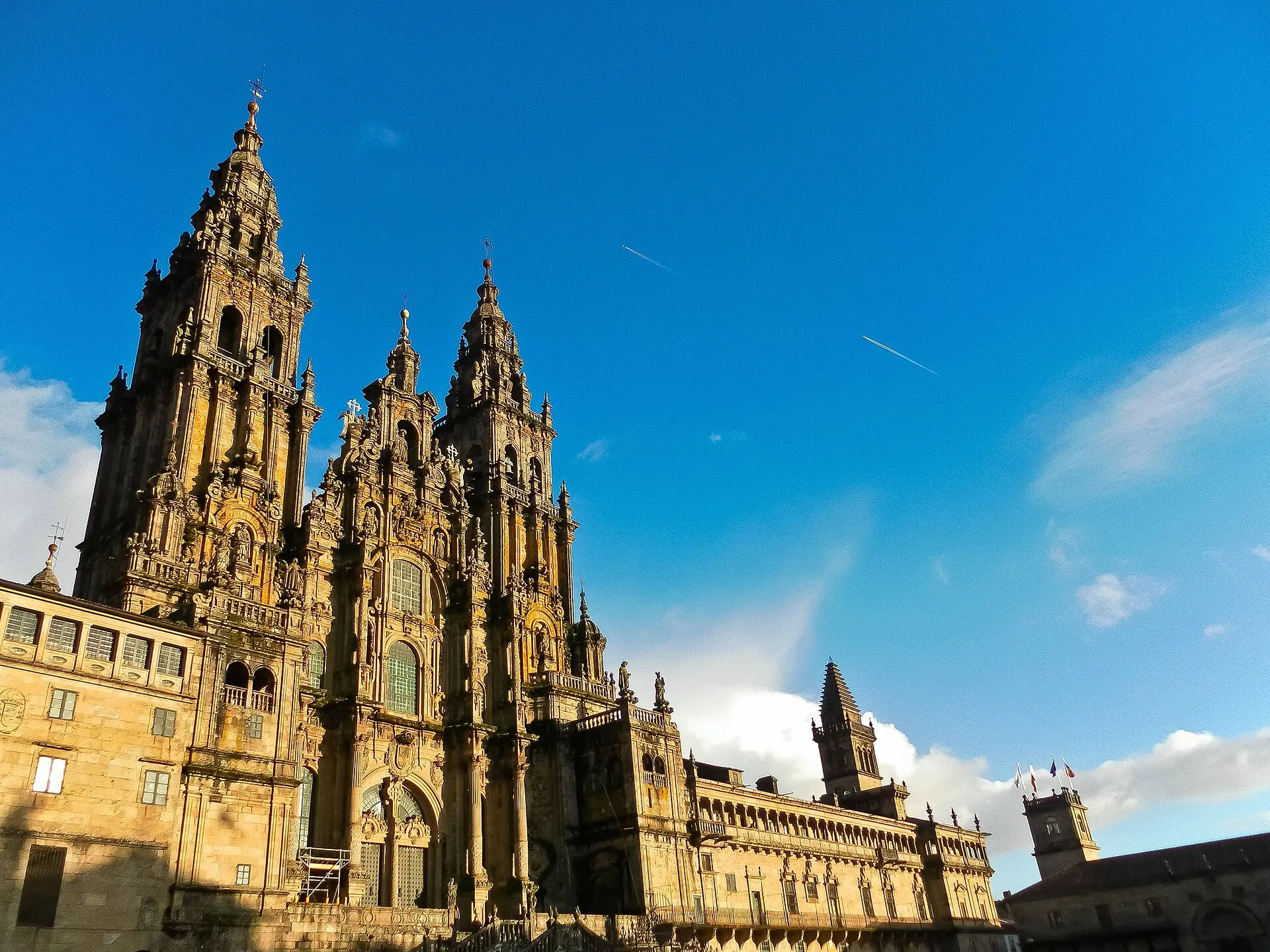 Barocke Obradoiro-Fassade der Kathedrale von Santiago de Compostela mit zwei Türmen in warmem Sonnenlicht vor blauem Himmel