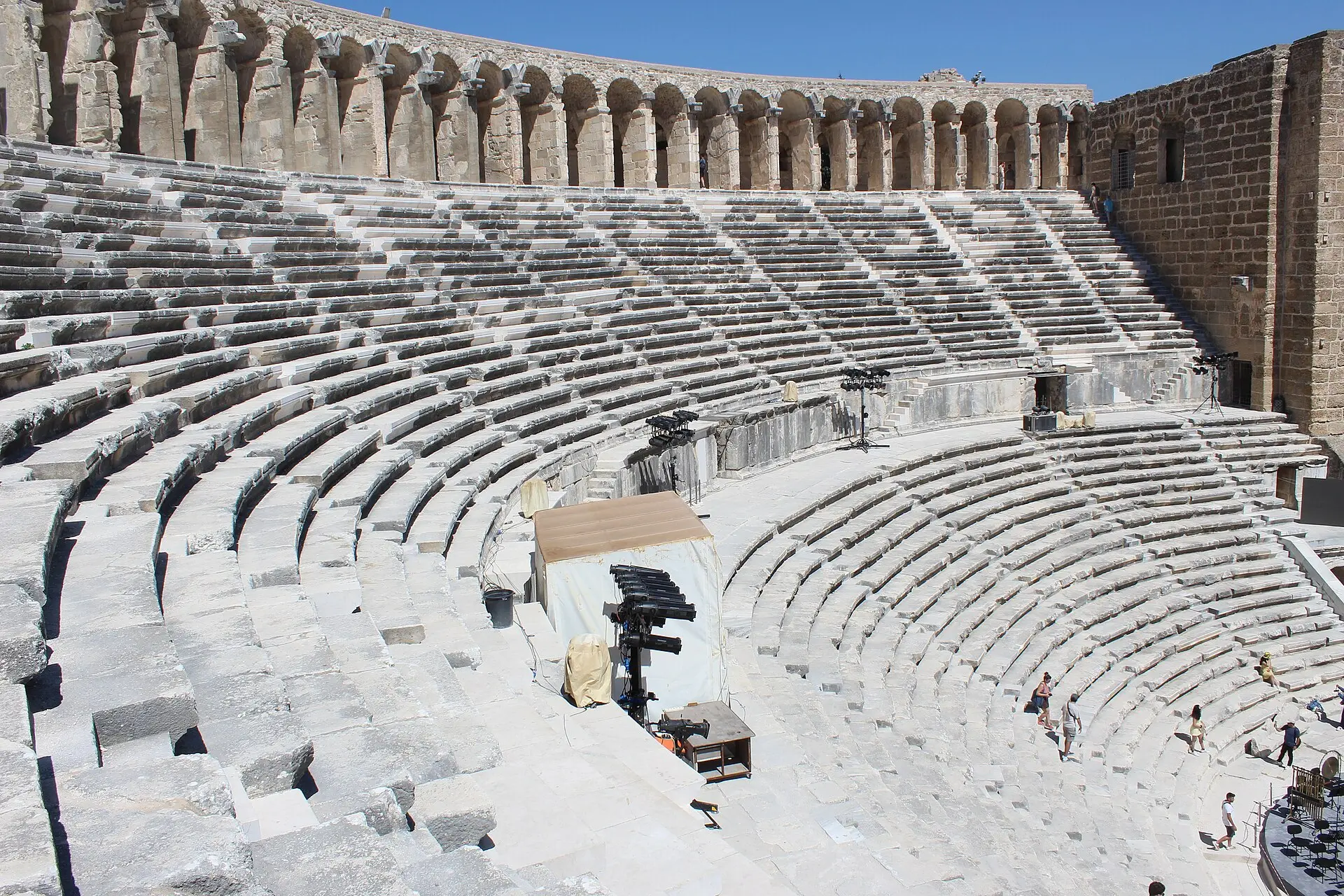 Halbrunde Sitzreihen im römischen Theater von Aspendos mit Bogengalerie am oberen Rand, rechts das Bühnenhaus, vorn Festivaltechnik
