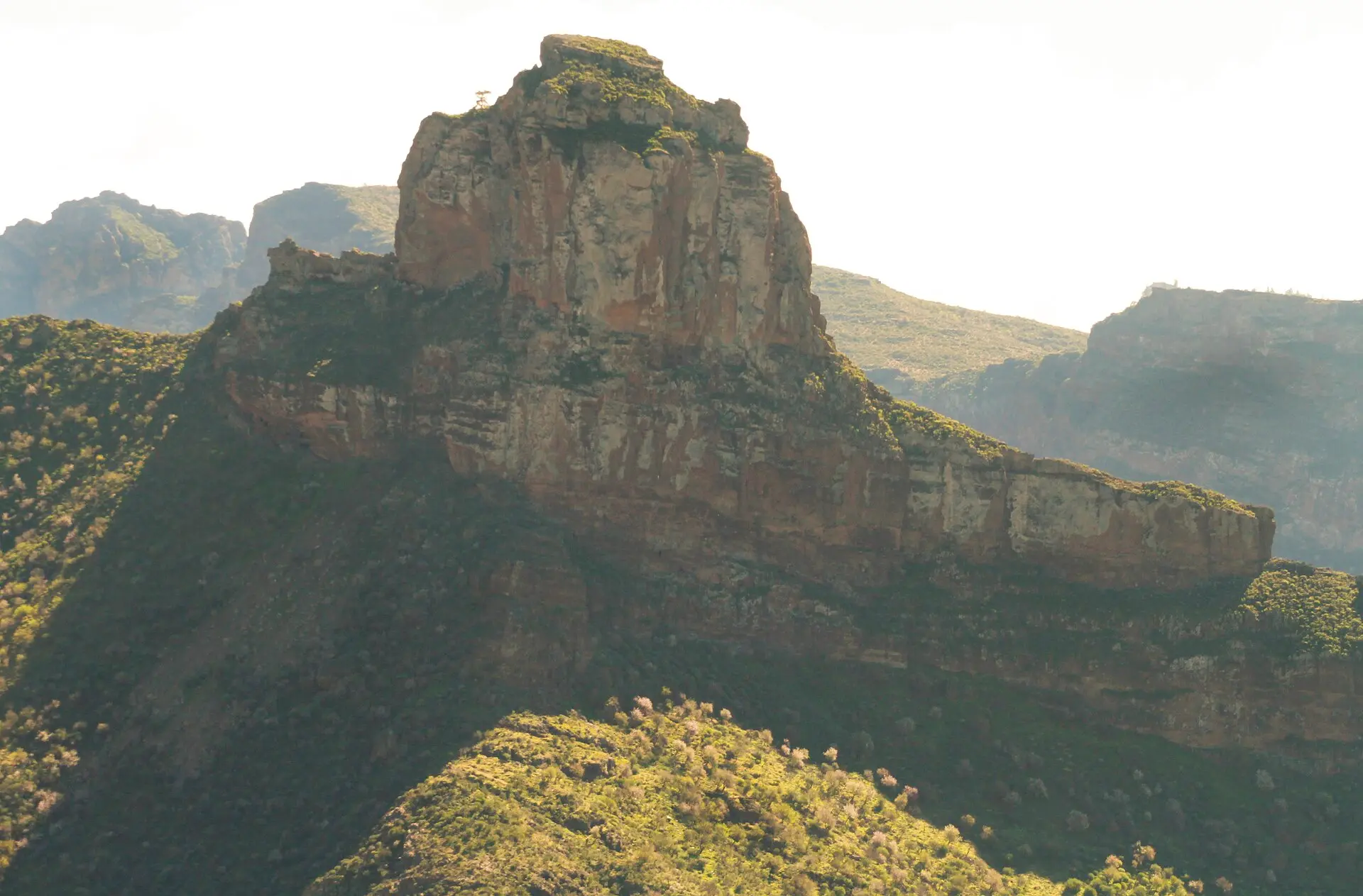 Der Felsblock Roque Bentayga von Artenara aus, mit geschichteten Felswänden und grünen Hängen im Gegenlicht