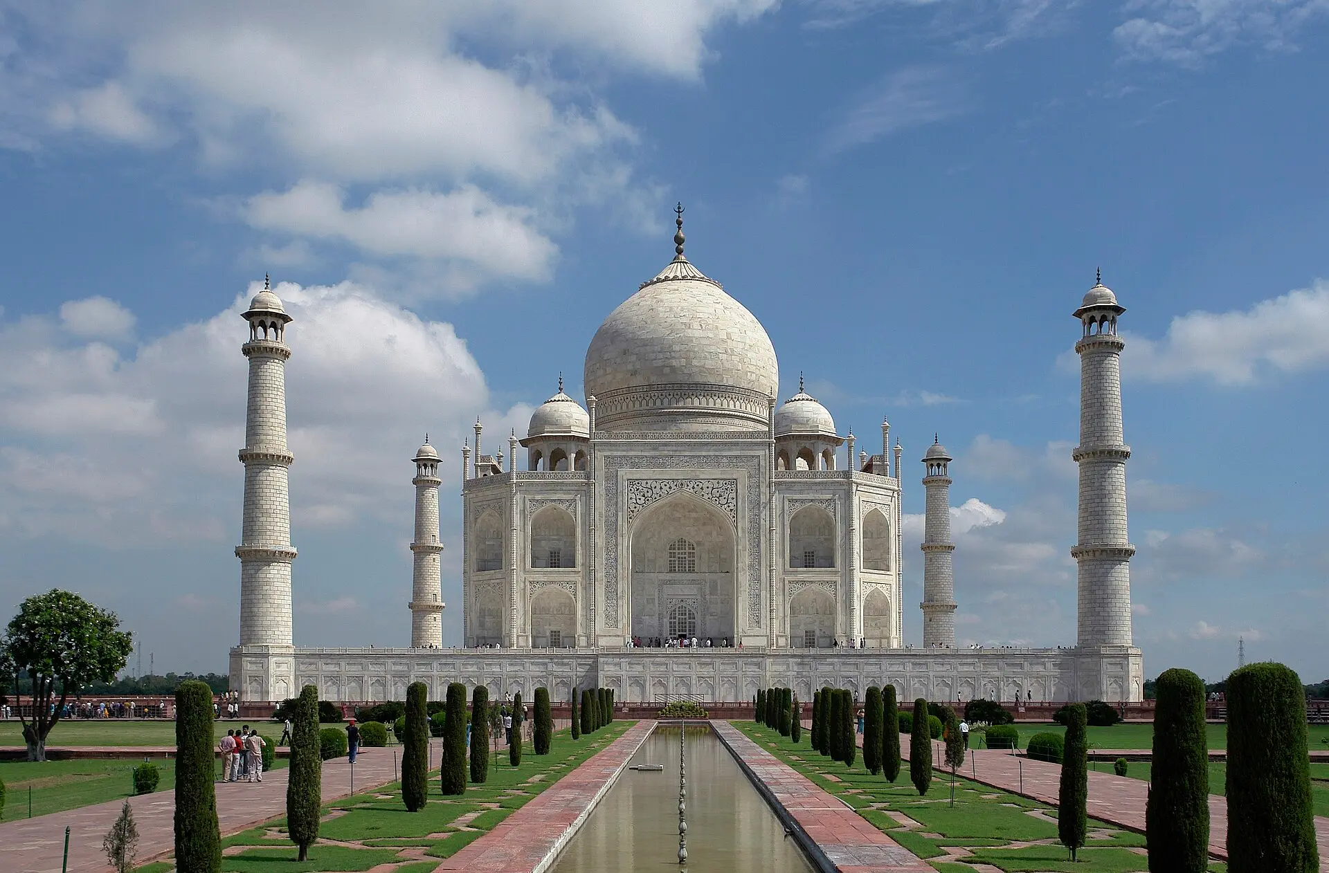 Taj Mahal in Agra von Süden: weiße Marmorkuppel mit vier Minaretten, davor ein langes Wasserbecken zwischen Zypressen und Rasen