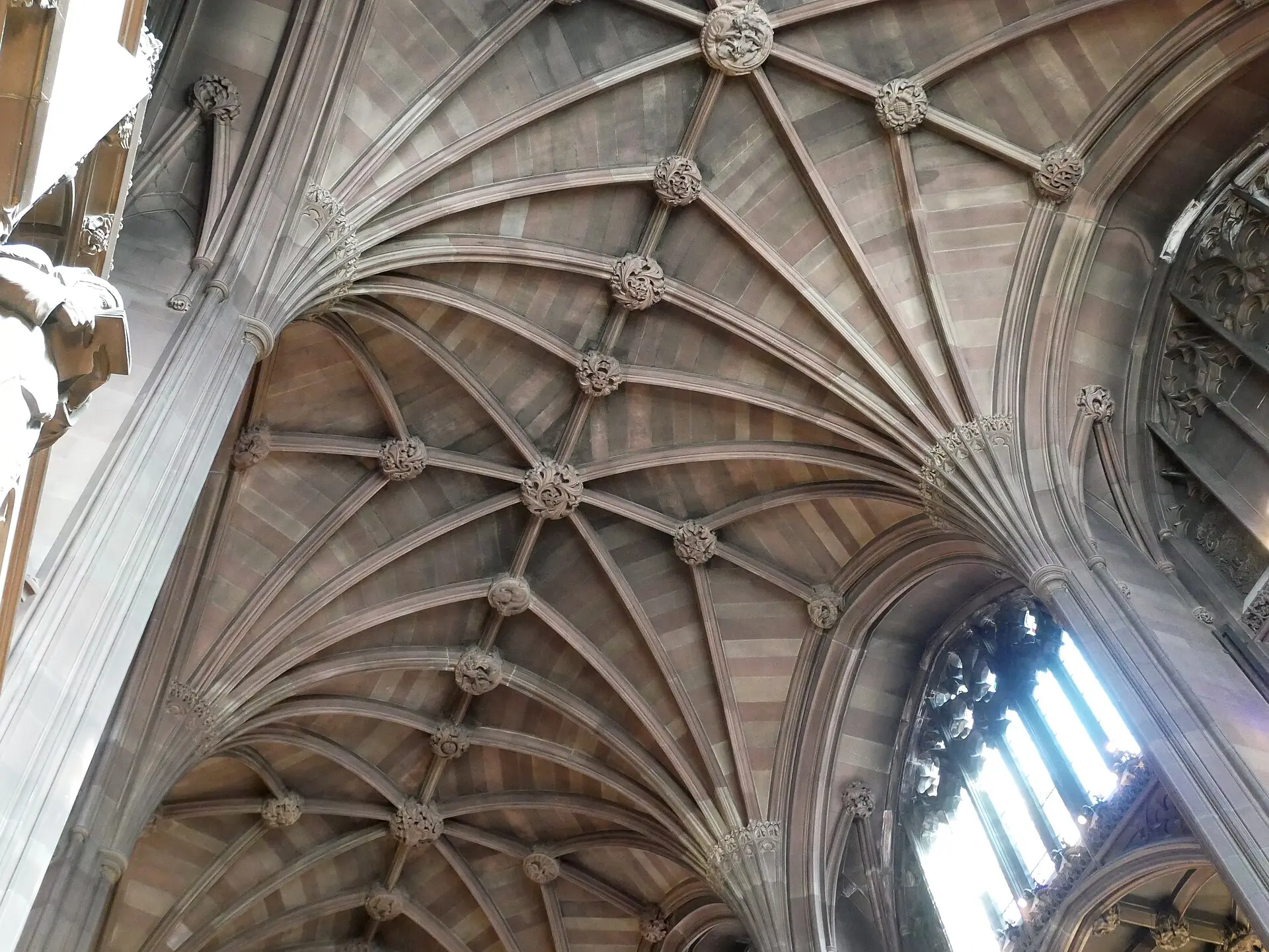 Neugotisches Rippengewölbe aus rötlichem Sandstein im Lesesaal der John Rylands Library, rechts ein hohes Maßwerkfenster