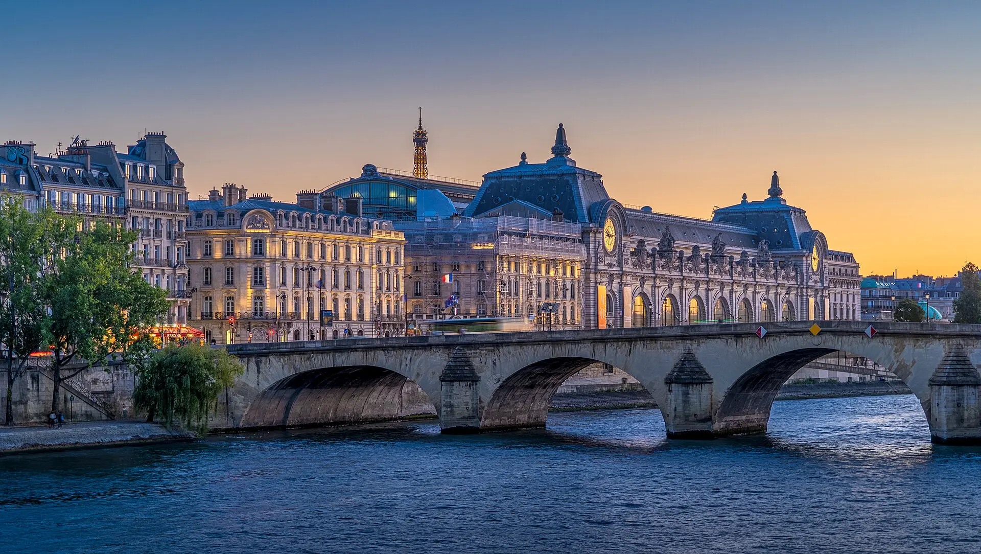 Pont Royal über der Seine zur blauen Stunde, dahinter das Musée d'Orsay mit seinen zwei Uhren unter orange-blauem Himmel