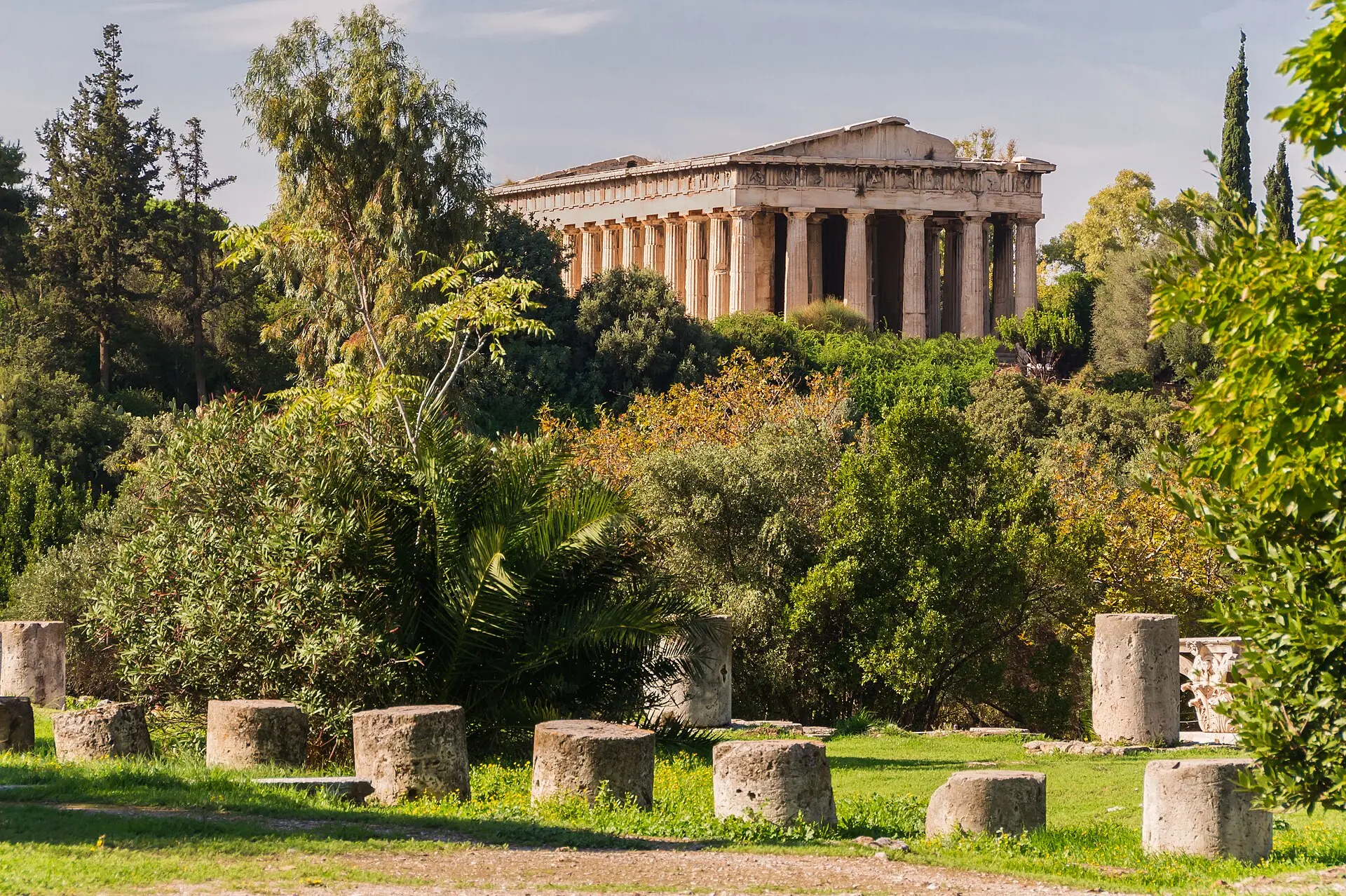 Hephaistos-Tempel auf dem Hügel über der Antiken Agora, davor Bäume, eine Palme und eine Wiese mit Säulenstümpfen
