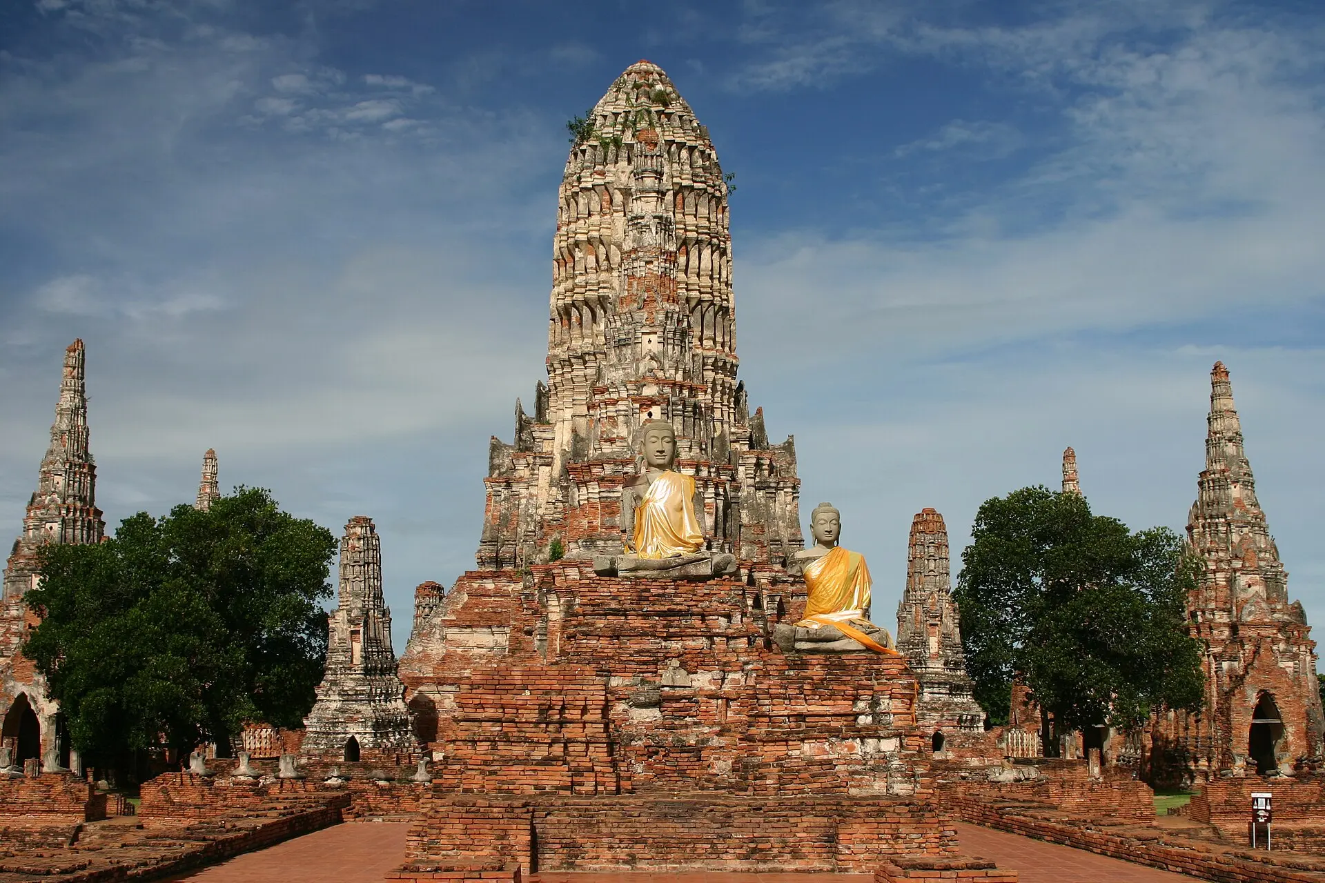 Tempelruine Wat Chaiwatthanaram in Ayutthaya: Prang aus Backstein, davor zwei sitzende Buddhafiguren mit orangefarbenen Schärpen