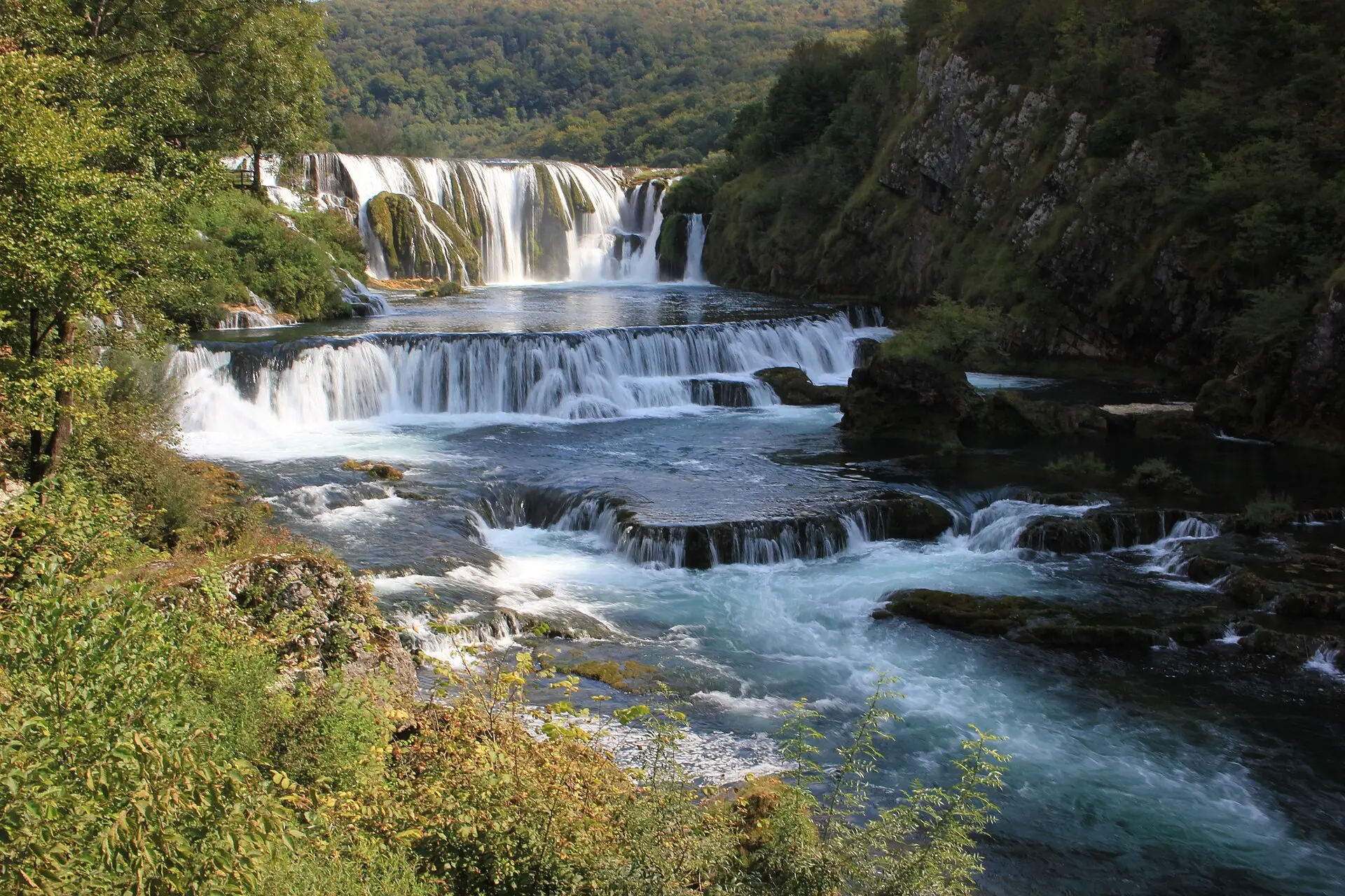 Stufenwasserfall Štrbački buk im Una-Nationalpark mit breiter Hauptkaskade, niedrigen Sinterstufen und bewaldetem Felshang