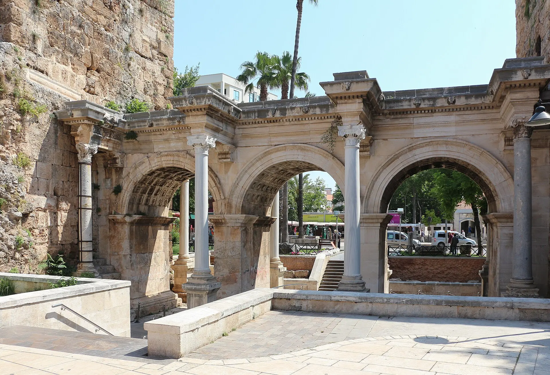 Hadrianstor in Antalya: drei Bögen aus weißem Marmor mit Säulen, links ein Turm, durch die Bögen der Blick auf eine Straße
