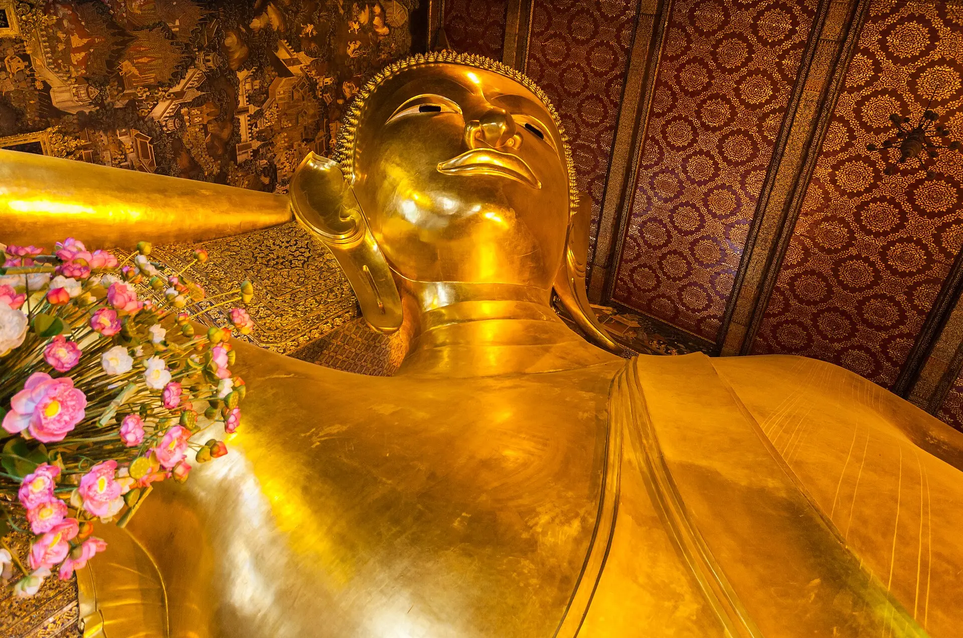 Kopf und Oberkörper des vergoldeten Liegenden Buddha im Wat Pho, links ein Gesteck aus rosa Lotusblüten