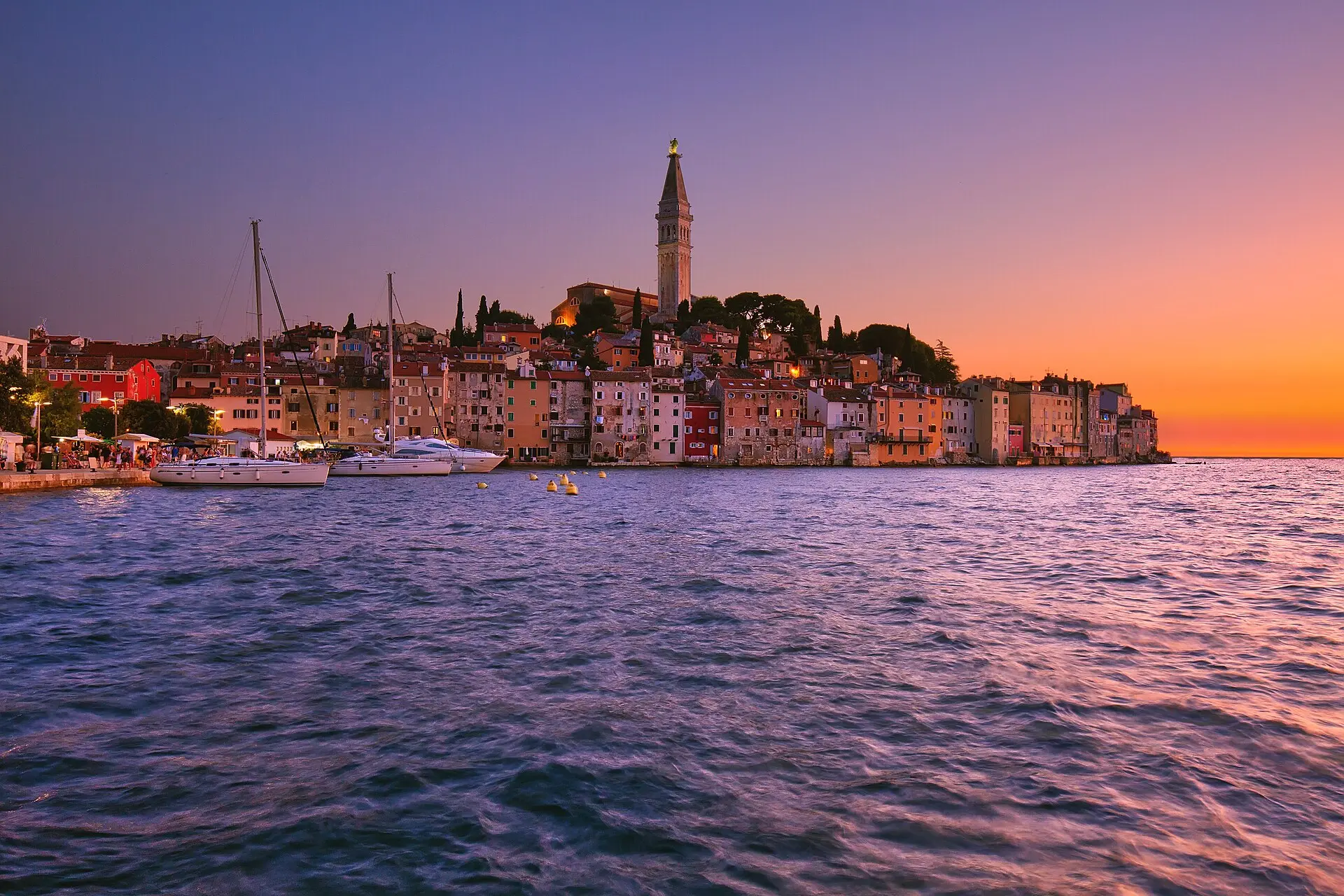 Altstadt von Rovinj auf ihrer Halbinsel bei Sonnenuntergang, bunte Häuser am Wasser, darüber der Glockenturm der hl. Euphemia