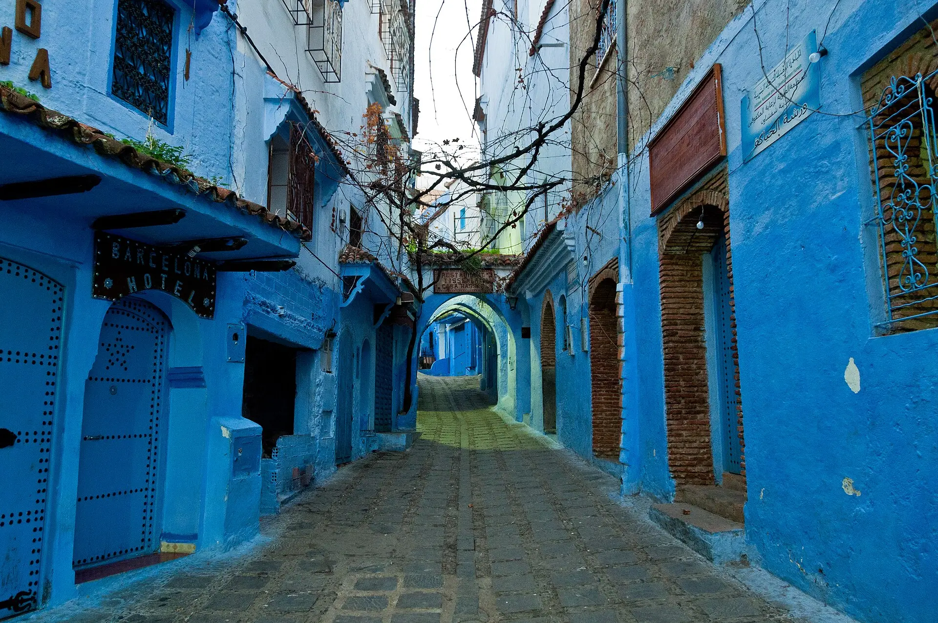 Menschenleere, gepflasterte Gasse in Chefchaouen zwischen blau gestrichenen Hauswänden, hinten blaue Rundbögen