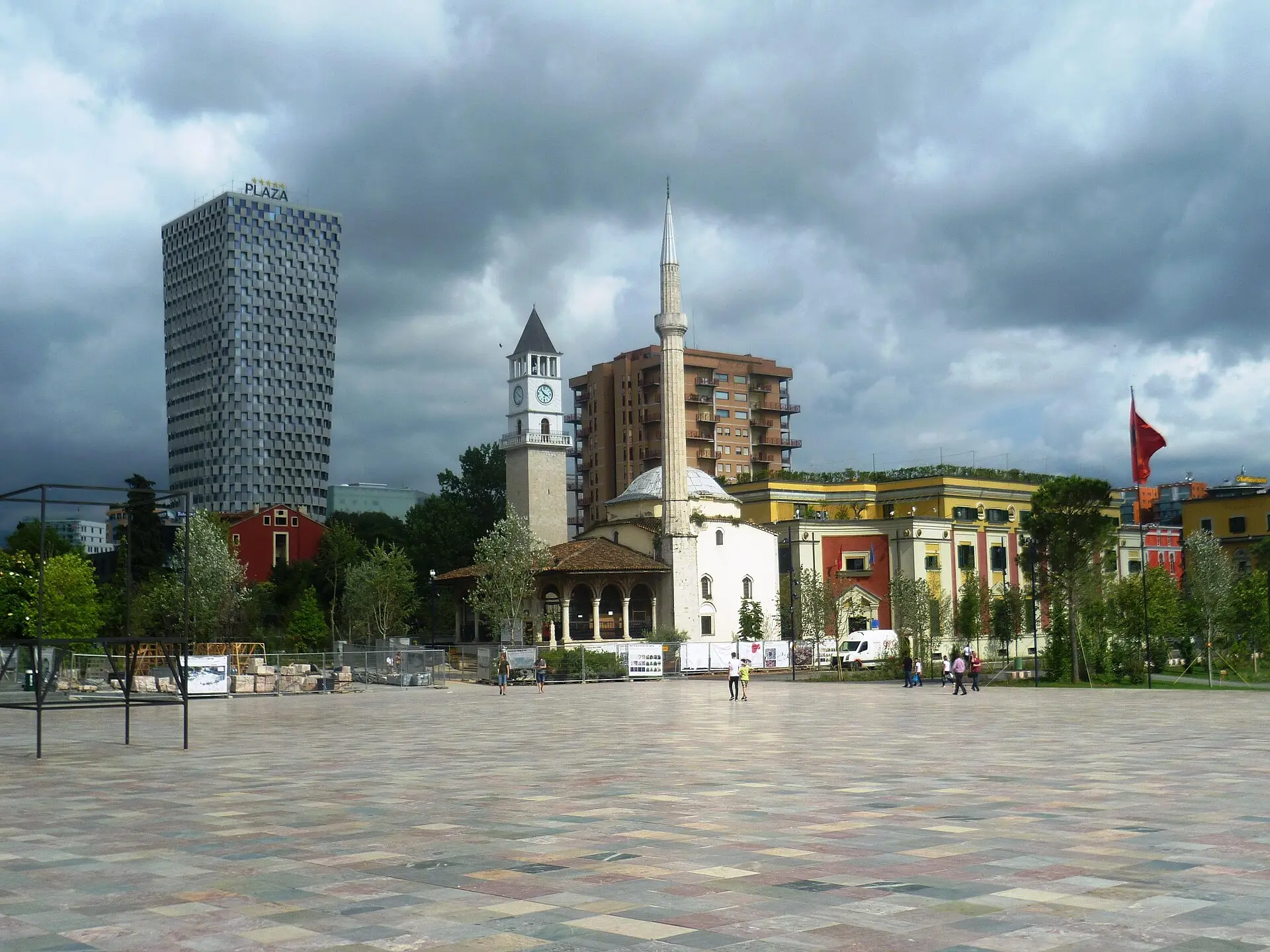 Skanderbeg-Platz in Tirana mit hellem Steinbelag, dahinter die Et’hem-Bey-Moschee mit Minarett und der Uhrturm unter Wolken
