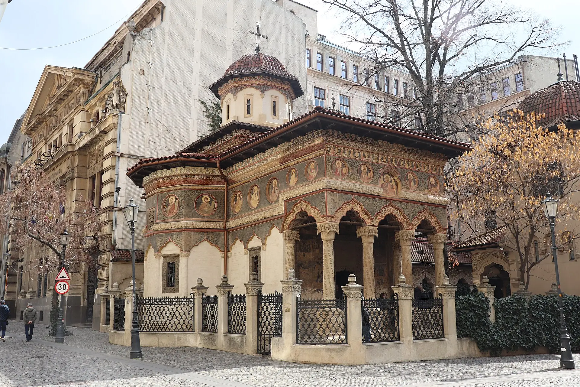 Kirche des Klosters Stavropoleos von der Straßenecke: Säulenvorhalle mit gemalten Medaillons, Kuppelturm, Eisenzaun und Bäume