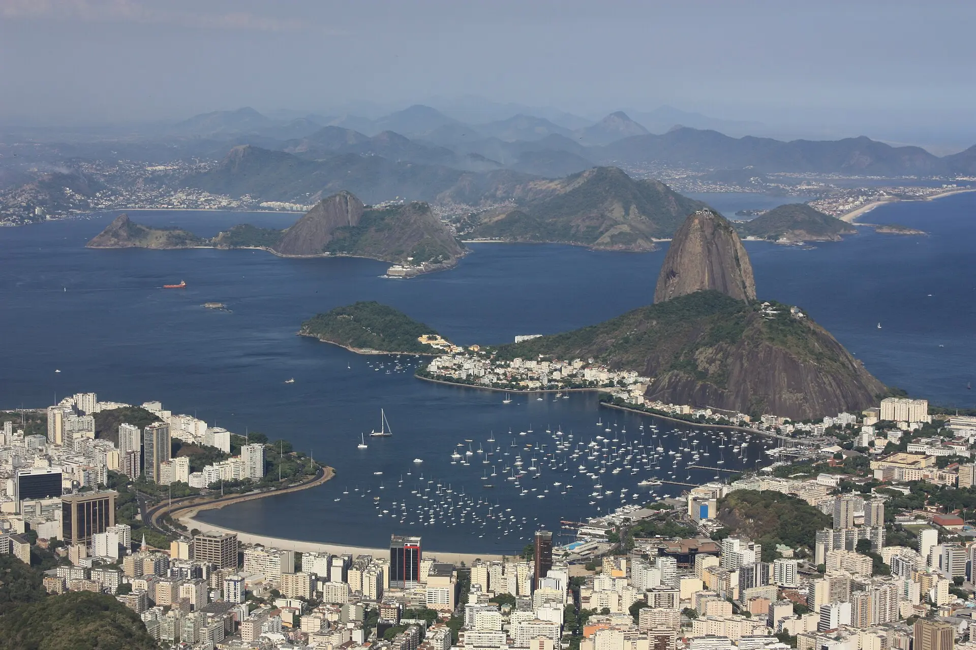Blick vom Corcovado über die Bucht von Botafogo mit Segelbooten auf den Zuckerhut, vorn Hochhäuser, hinten Berge im Dunst