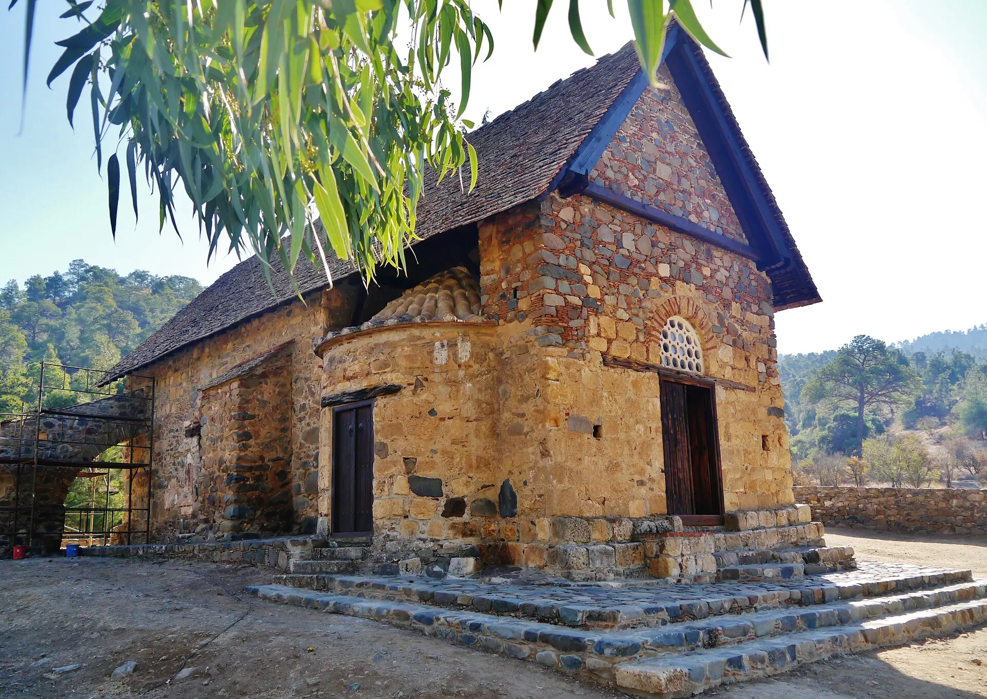 Kleine Bruchsteinkirche Panagia tis Asinou mit steilem Ziegeldach und rundem Vorbau mit Kuppel, dahinter bewaldete Hügel