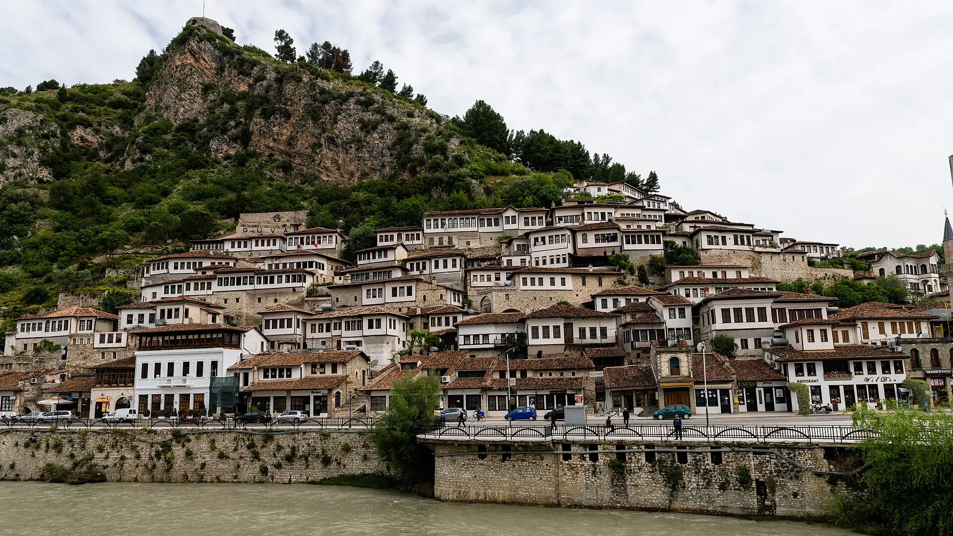 Viertel Mangalem in Berat: weiße Häuser mit vielen Fensterreihen am Hang, davor der Fluss Osum und eine Uferstraße